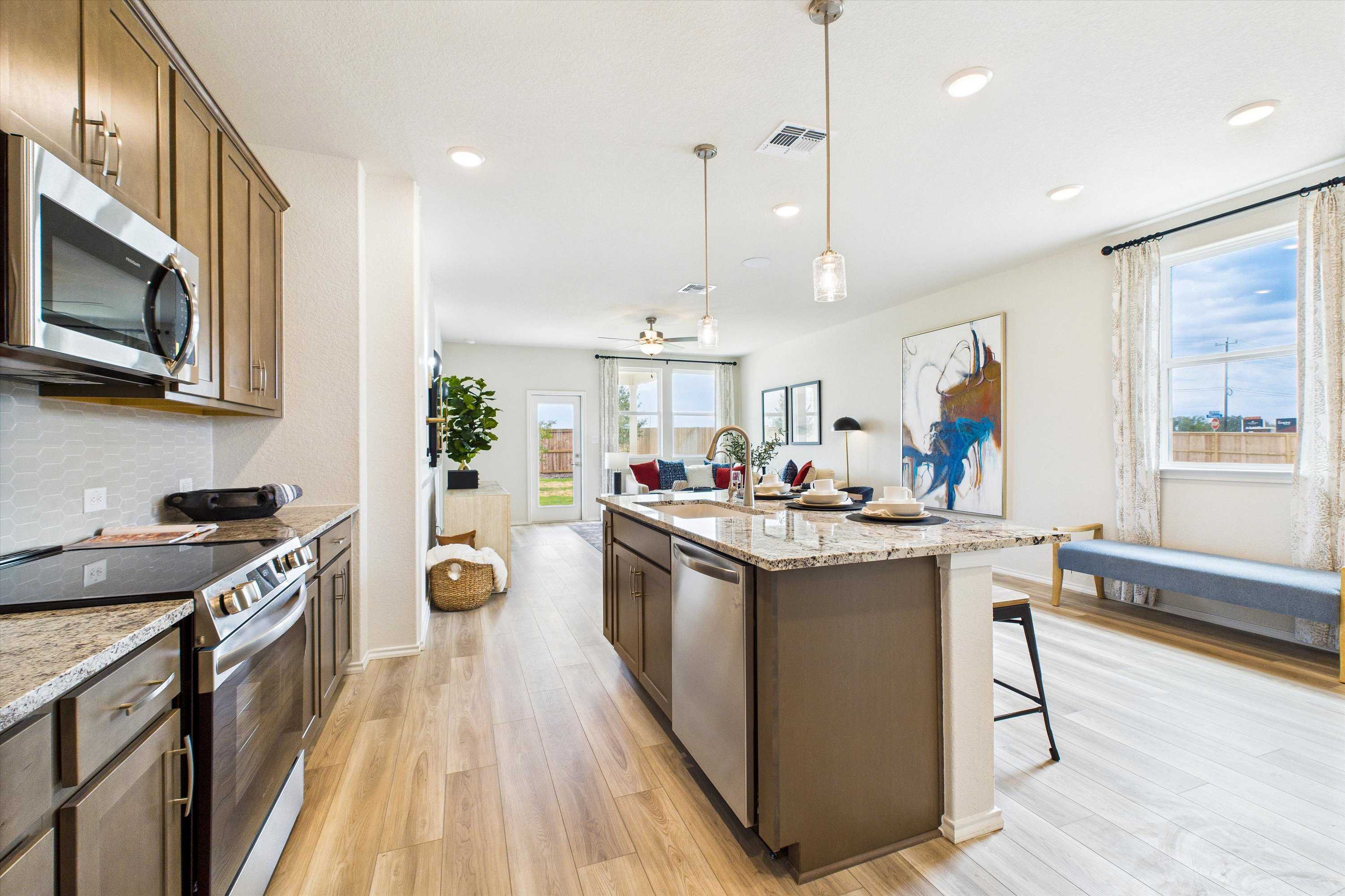 Open-concept kitchen and living room in Fairway Crossing Converse TX by Davidson Homes featuring granite island, hardwood floors, large windows
