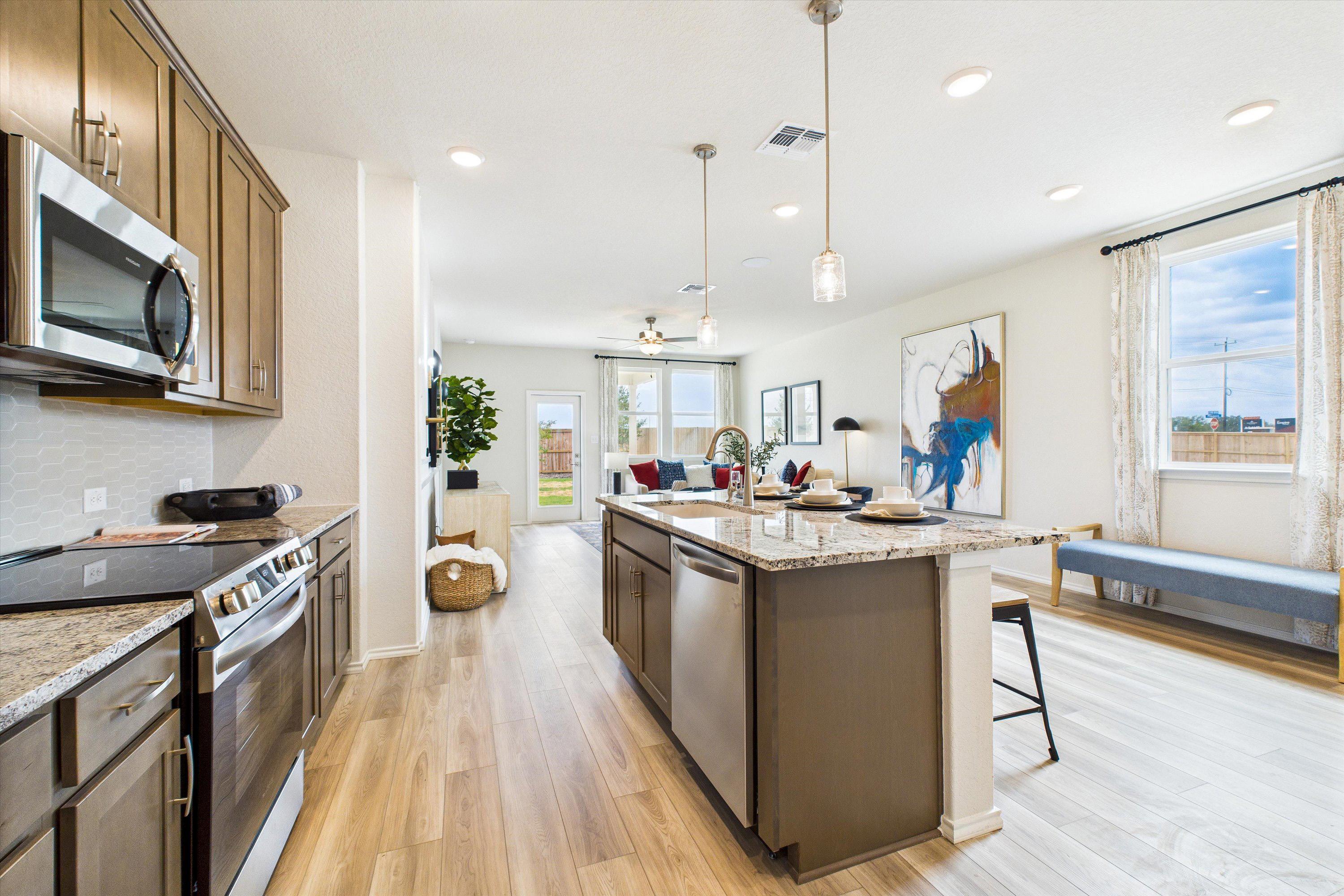 Open-concept kitchen and living room in Fairway Crossing Converse TX by Davidson Homes featuring granite island, hardwood floors, large windows