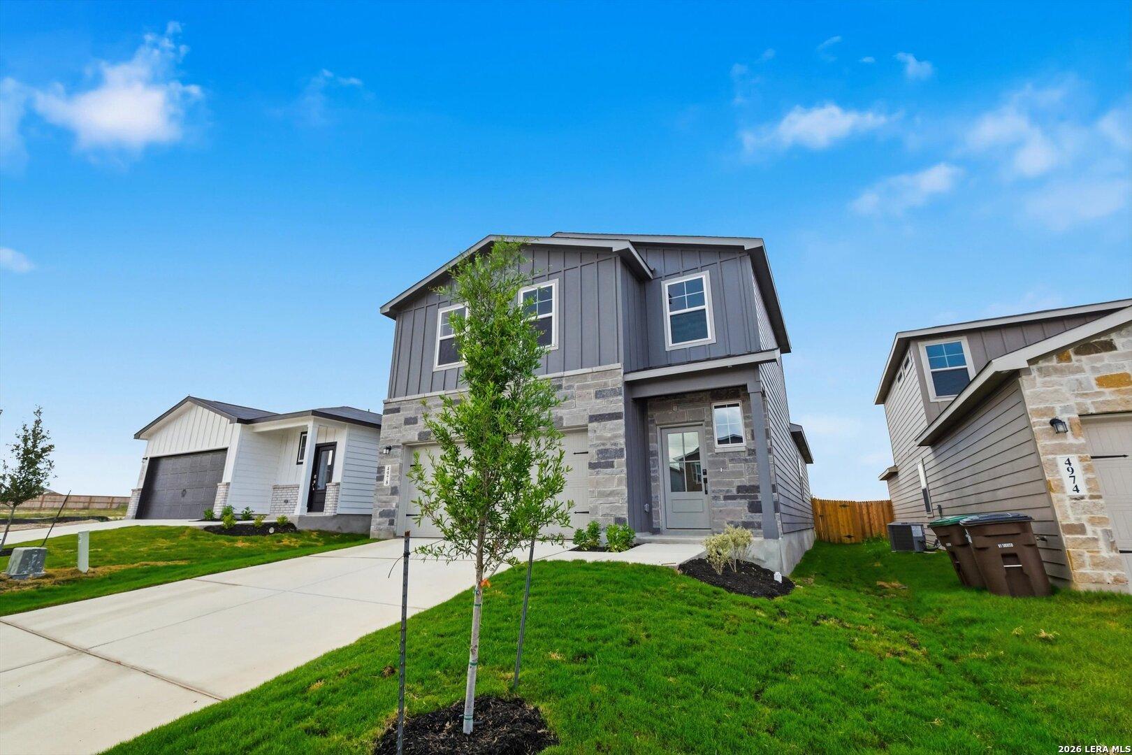 Modern 2-story gray home with stone accents, 2-car garage, driveway, and lush green yard in Agave, San Antonio, Texas - Davidson Homes Blanco C