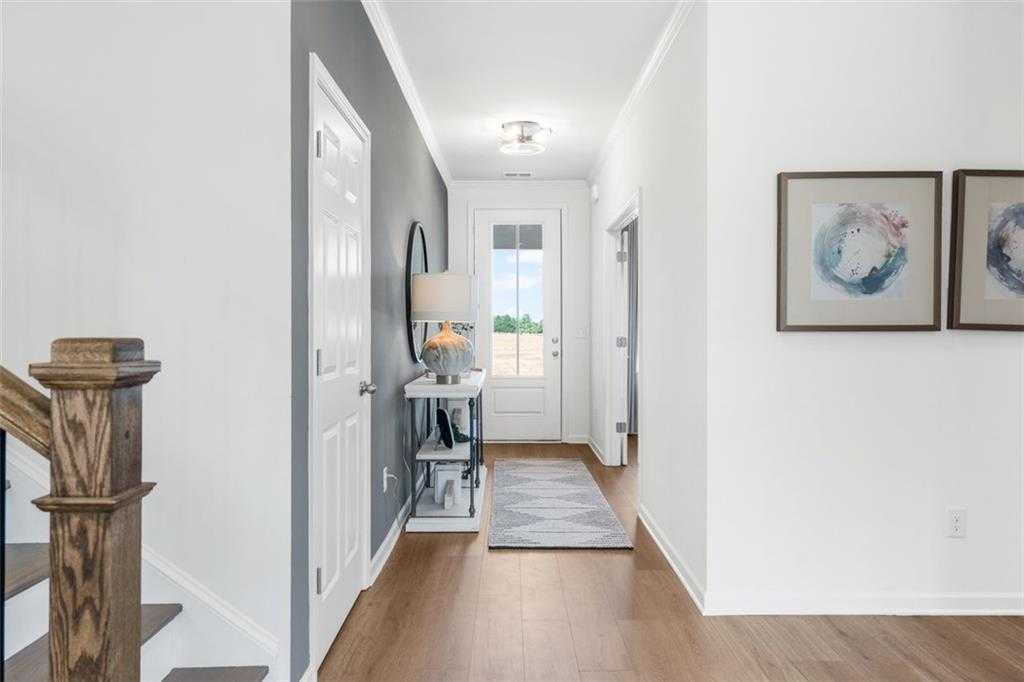 Bright entry hallway with oak staircase, console table, mirror, and abstract art in 5-bedroom Davidson Homes, Hoschton, GA