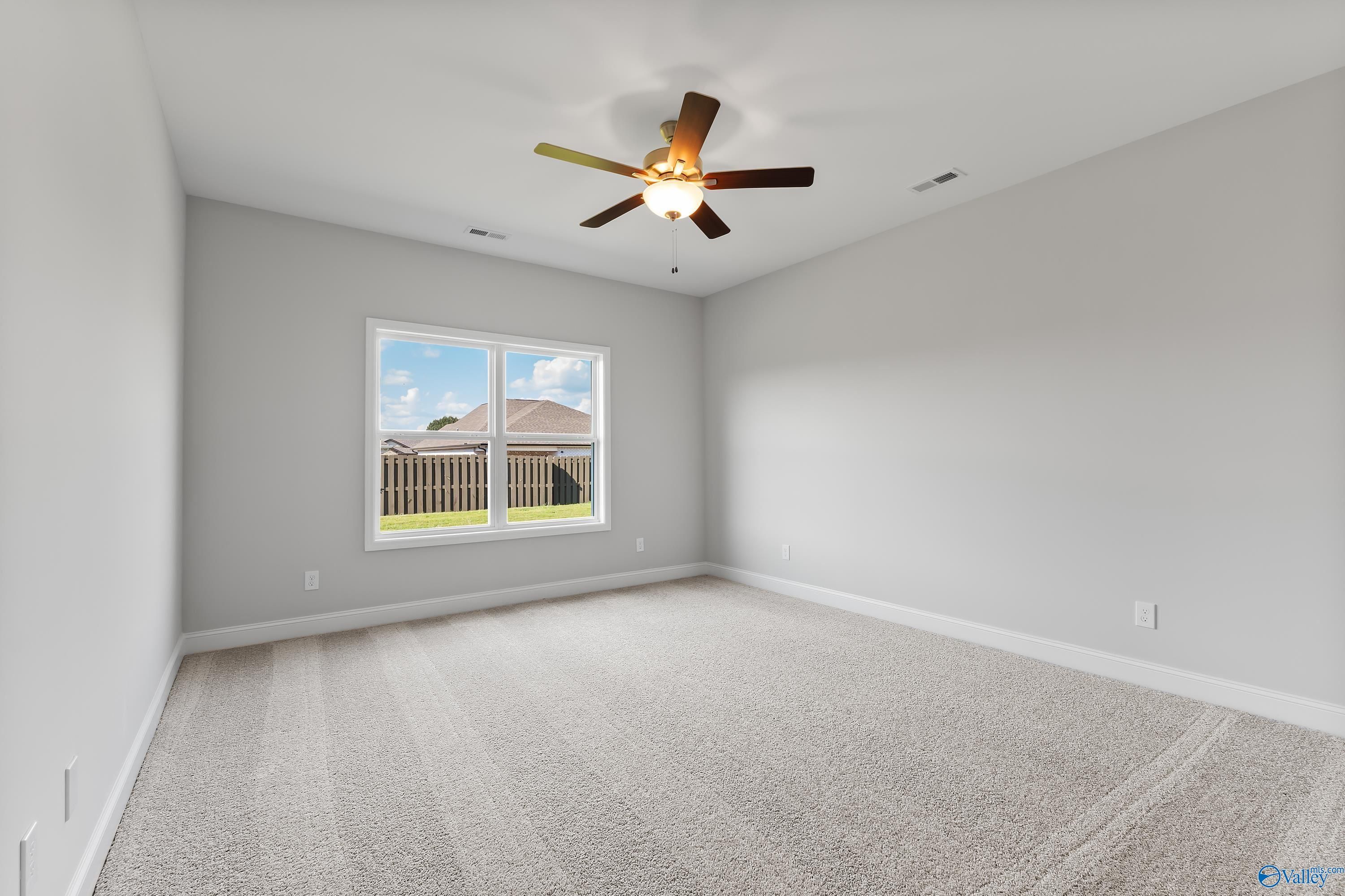 Spacious secondary bedroom with gray walls, ceiling fan, and window view of fenced backyard in Davidson Homes The Daphne, Hazel Green, Alabama