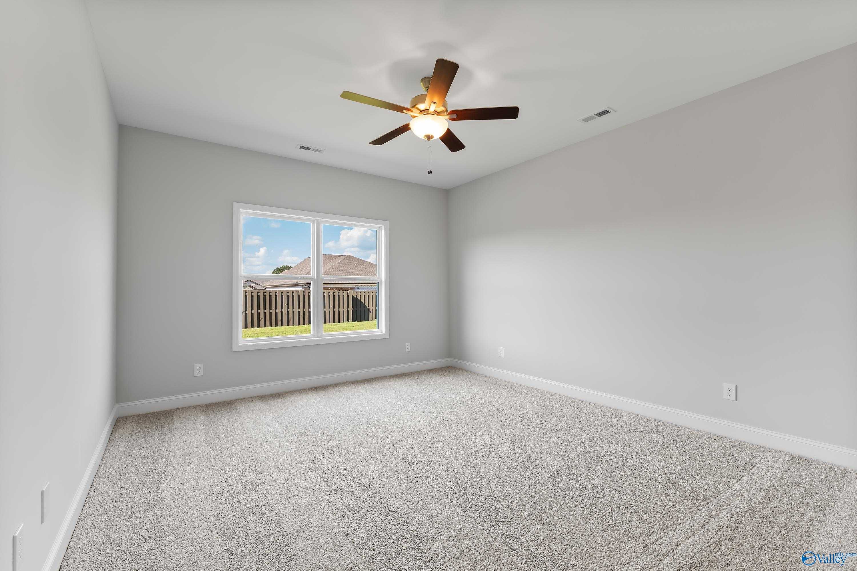 Spacious secondary bedroom with gray walls, ceiling fan, and window view of fenced backyard in Davidson Homes The Daphne, Hazel Green, Alabama