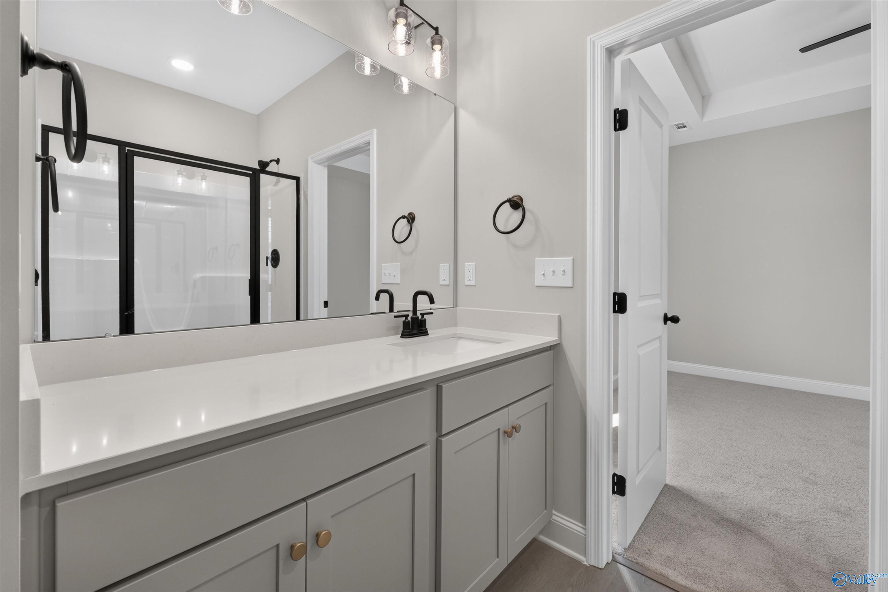 Modern bathroom with gray vanity, quartz countertop, black fixtures, and framed mirror in Davidson Homes The Butler, Hazel Green, Alabama
