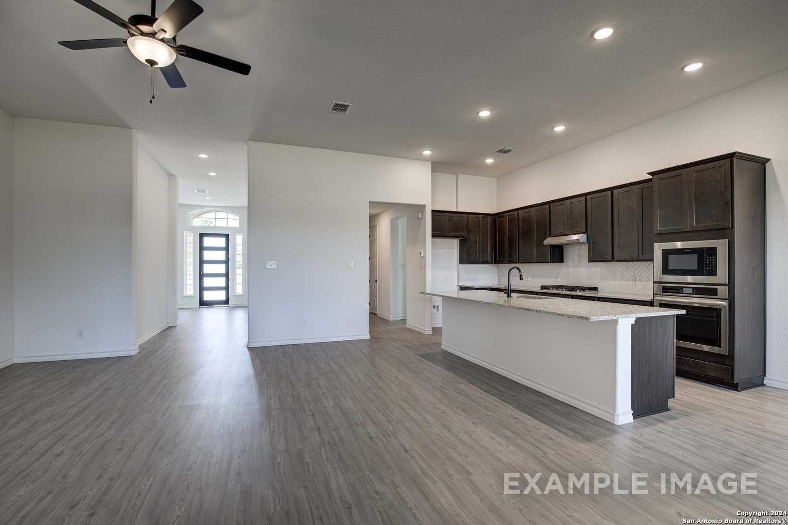 Open-concept kitchen with dark wood cabinets, white island, stainless appliances, and hardwood floors in The Garner C, Castroville, Texas