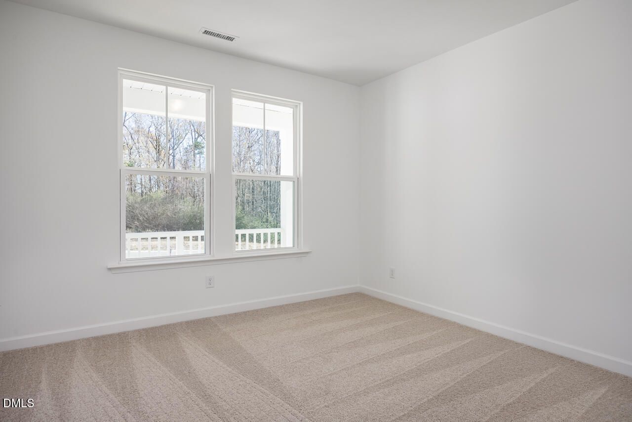Bright upstairs bedroom with large windows, beige carpet, and balcony view of trees in Davidson Homes The Cypress B II, Angier, NC