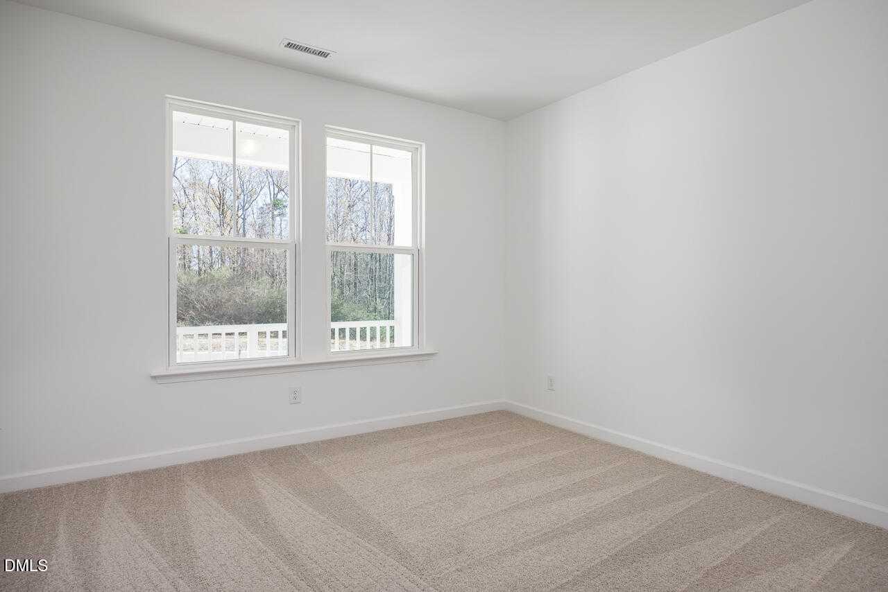 Bright upstairs bedroom with large windows, beige carpet, and balcony view of trees in Davidson Homes The Cypress B II, Angier, NC