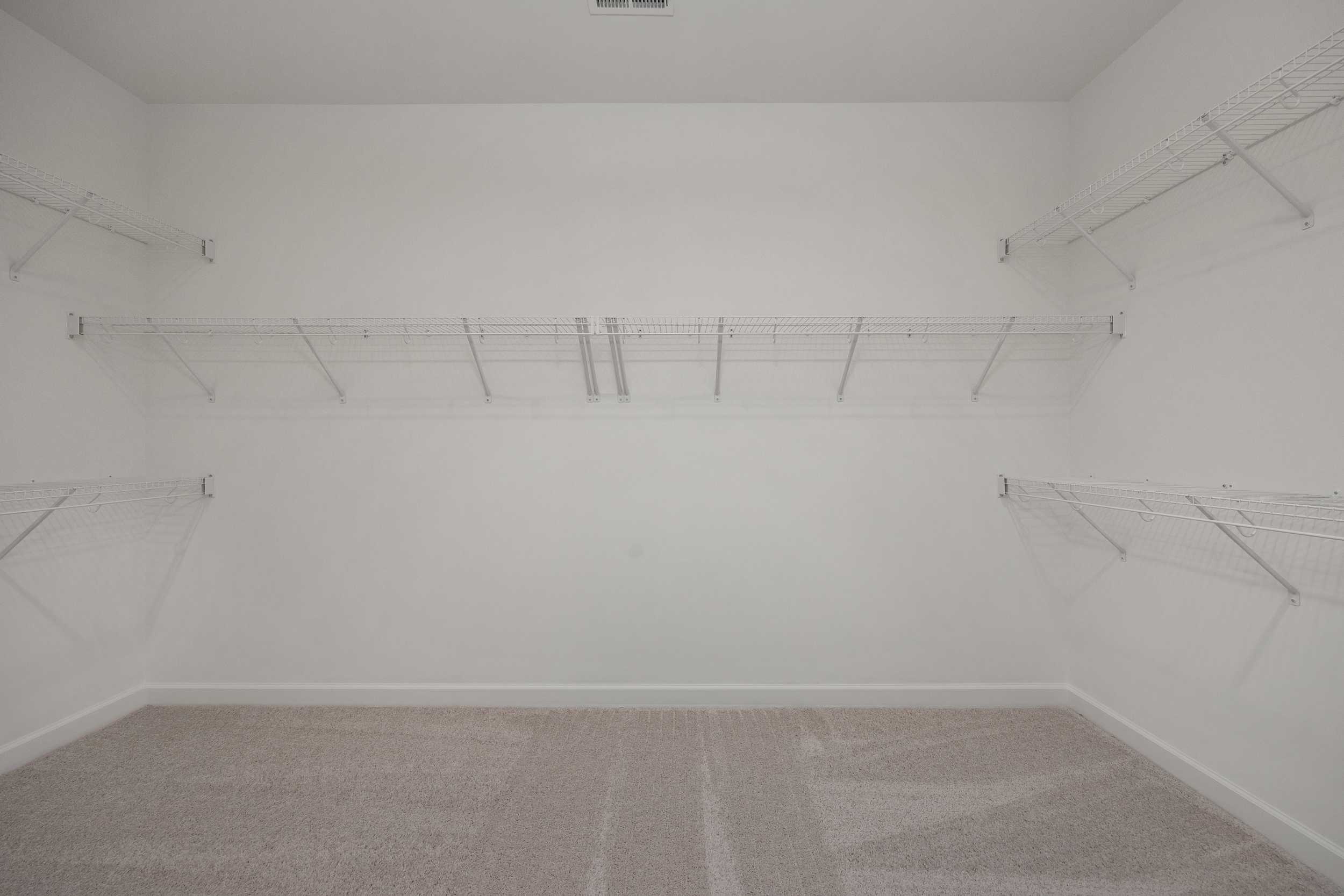 Spacious walk-in closet in The Hickory II master suite with wire shelving, white walls, and beige carpet
