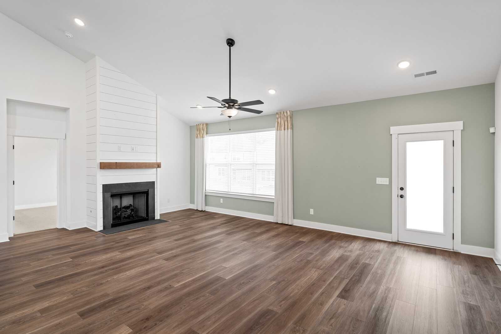 Cozy living room with shiplap fireplace, hardwood floors, ceiling fan and large windows in Davidson Homes The Ridgeport, Gallatin, TN