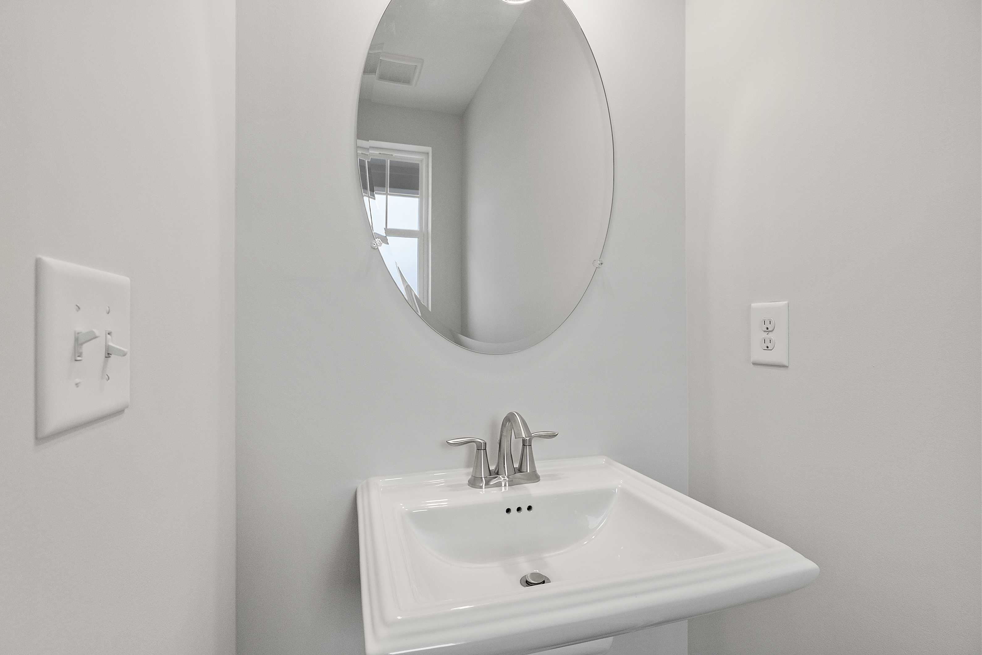 Modern powder room in The Durant A featuring oval mirror above white sink with chrome faucet