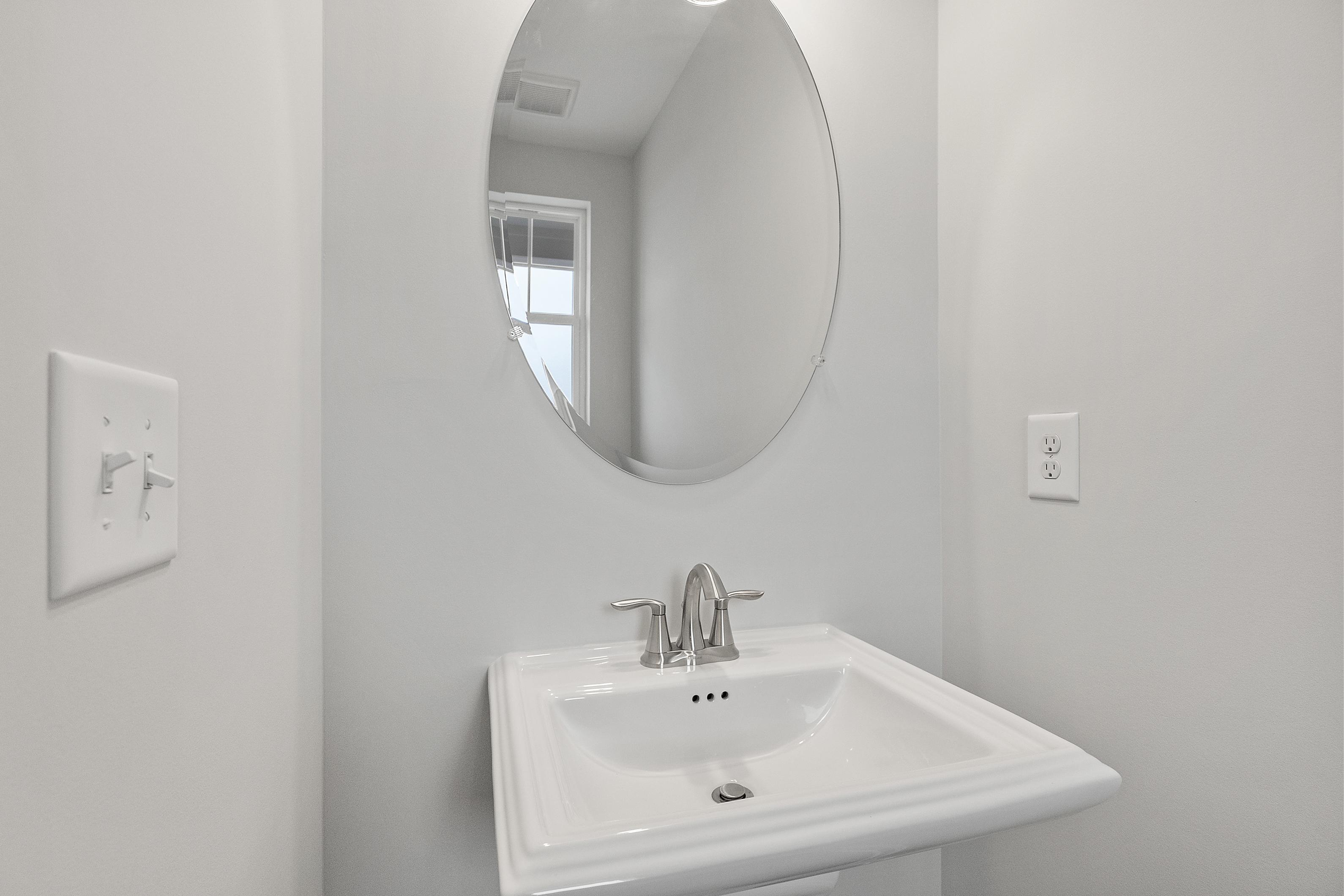 Modern powder room in The Durant A featuring oval mirror above white sink with chrome faucet