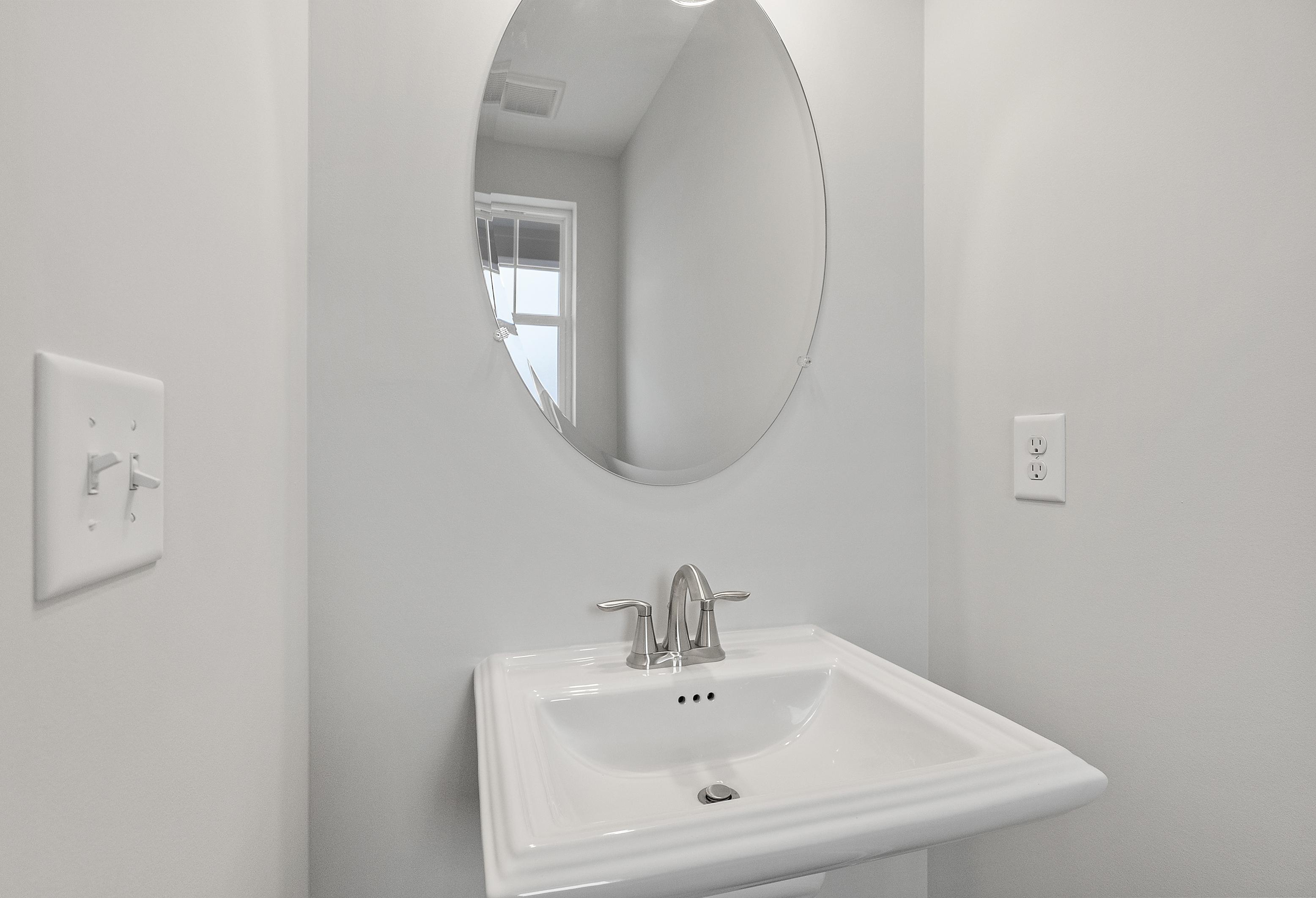 Modern powder room in The Durant A featuring oval mirror above white sink with chrome faucet