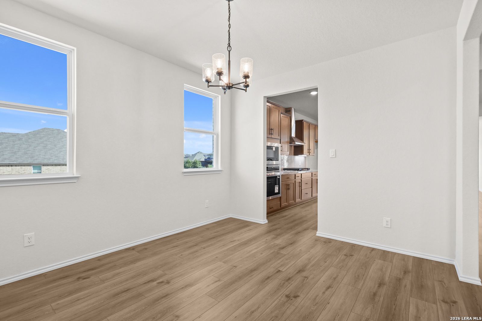 Bright dining room with wood-look flooring and chandelier adjoining kitchen in Davidson Homes Glenwood E, San Antonio, Texas