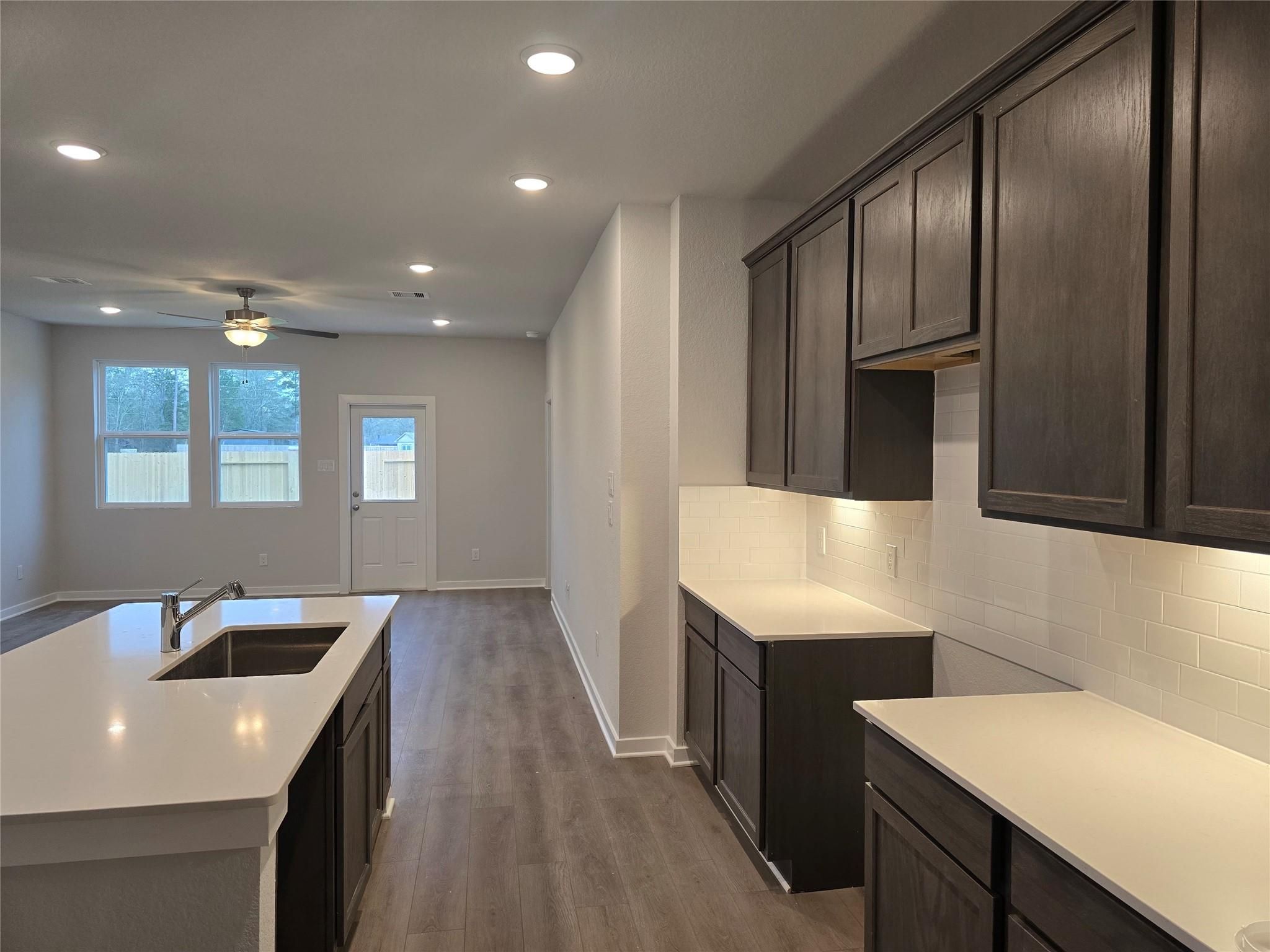 Open-concept kitchen with dark cabinets, quartz island sink, subway tile backsplash in Davidson Homes Brazos E, Cleveland Texas