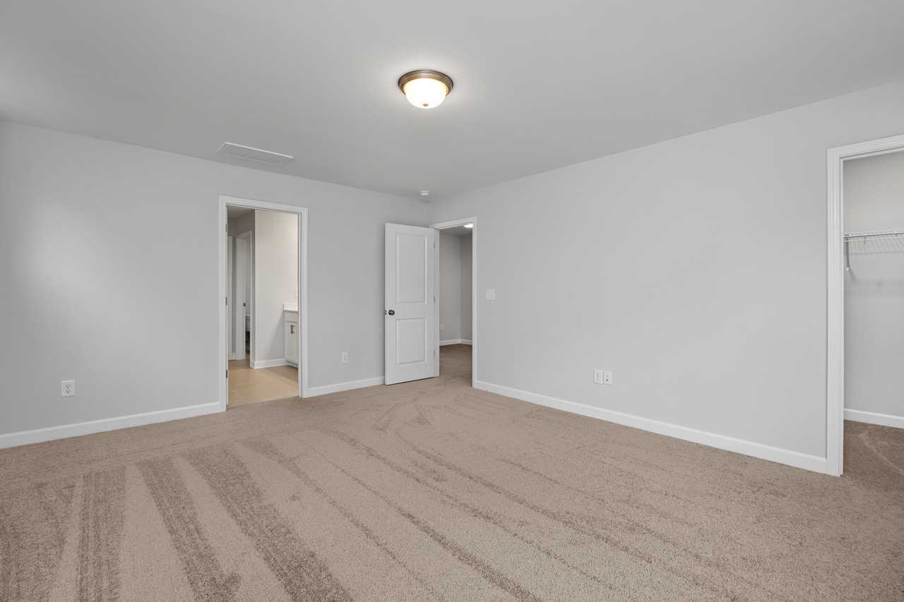Spacious master bedroom in The Durham with light gray walls, beige carpet, walk-in closet, and bathroom access