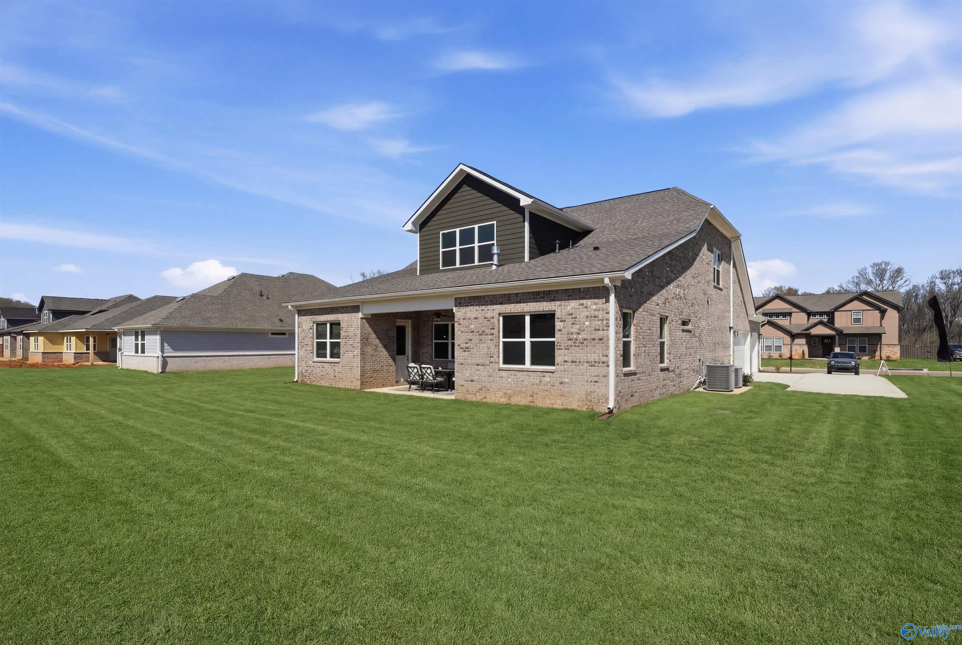 Modern 1.5-story brick home with dark siding, covered porch, and lush green lawn in The Meadows at Hampton Cove, Owens Cross Roads, AL