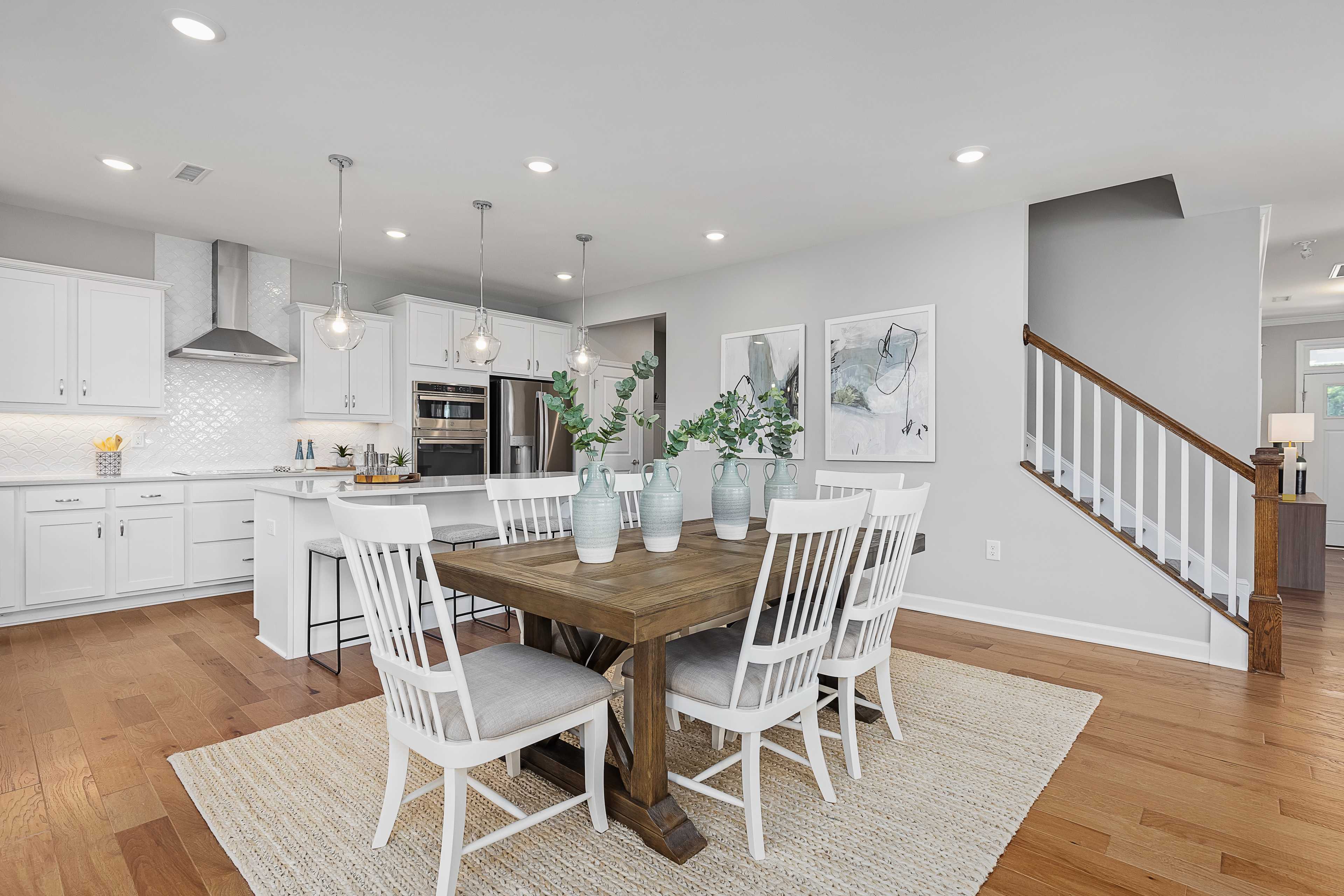 Open-concept kitchen and dining area at Woodland Crossing in Zebulon, NC with white cabinets, farmhouse table, and hardwood floors