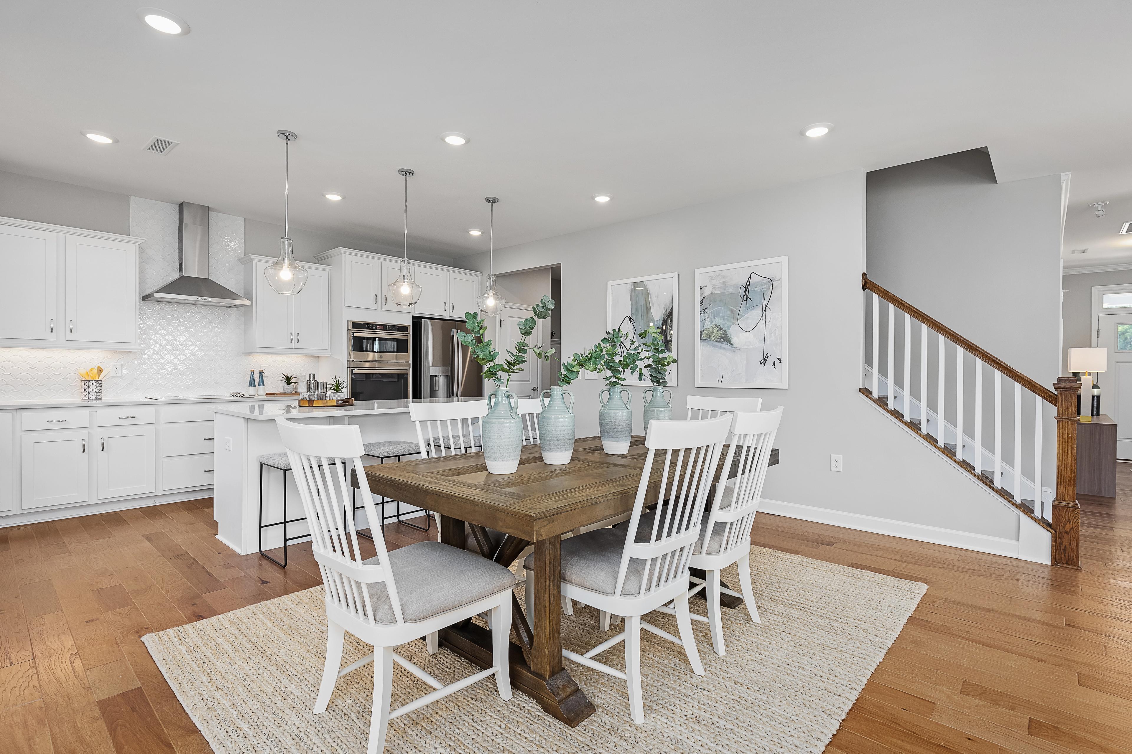 Open-concept kitchen and dining area at Woodland Crossing in Zebulon, NC with white cabinets, farmhouse table, and hardwood floors