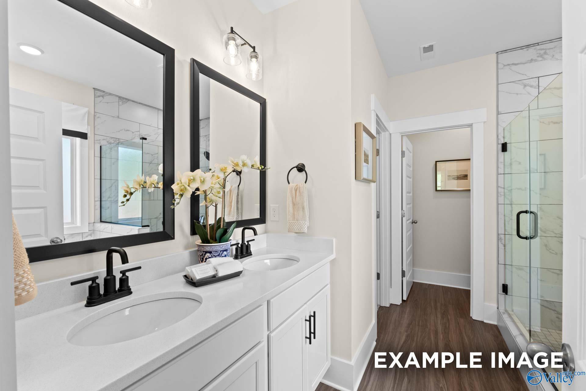 Elegant master bathroom with double vanity, white quartz counters, glass shower, and orchids in Davidson Homes The Daphne F, New Market, Alabama