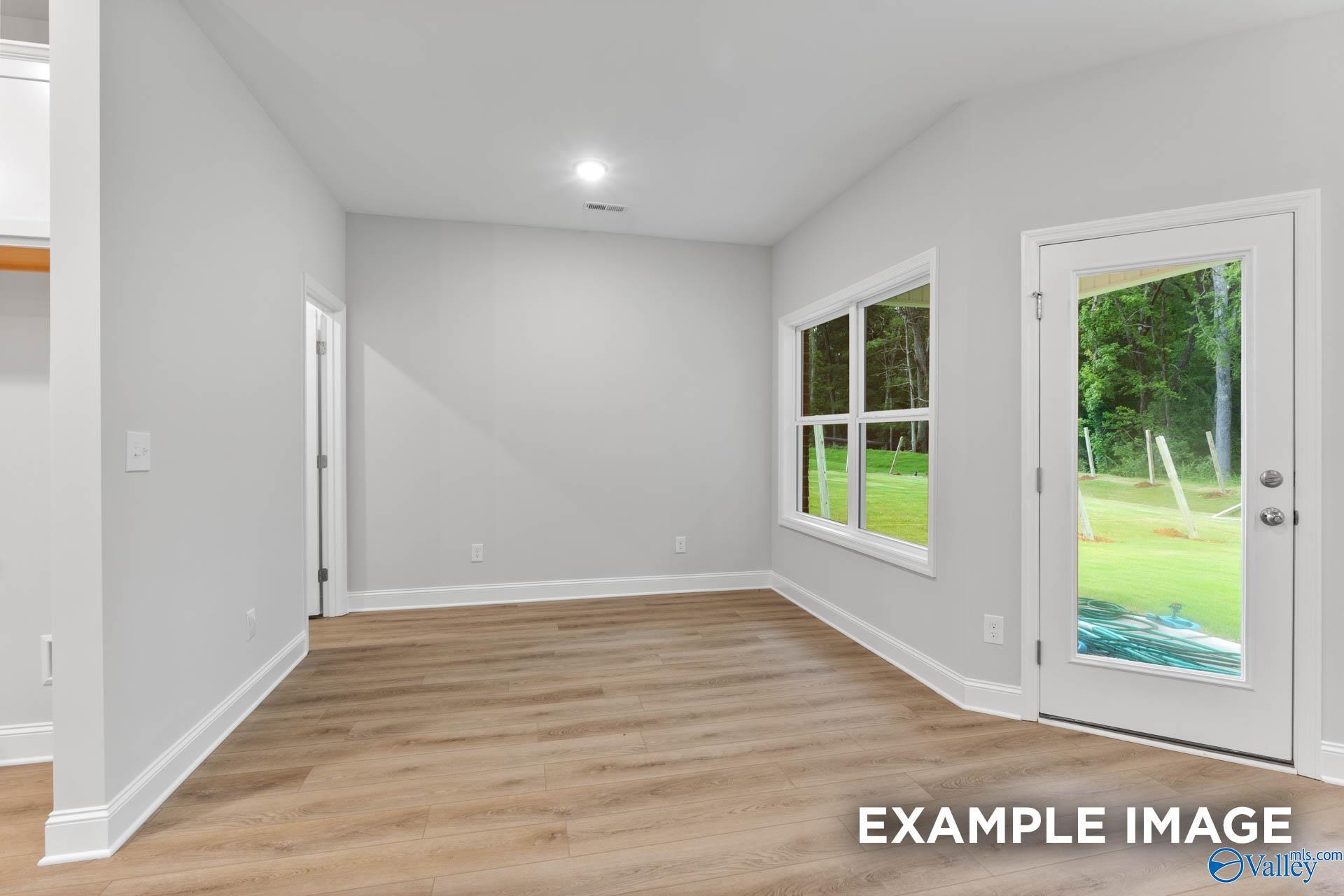 Bright empty living room with hardwood floors, large window, and glass door to green yard in Davidson Homes The Daphne, Meridianville, Alabama