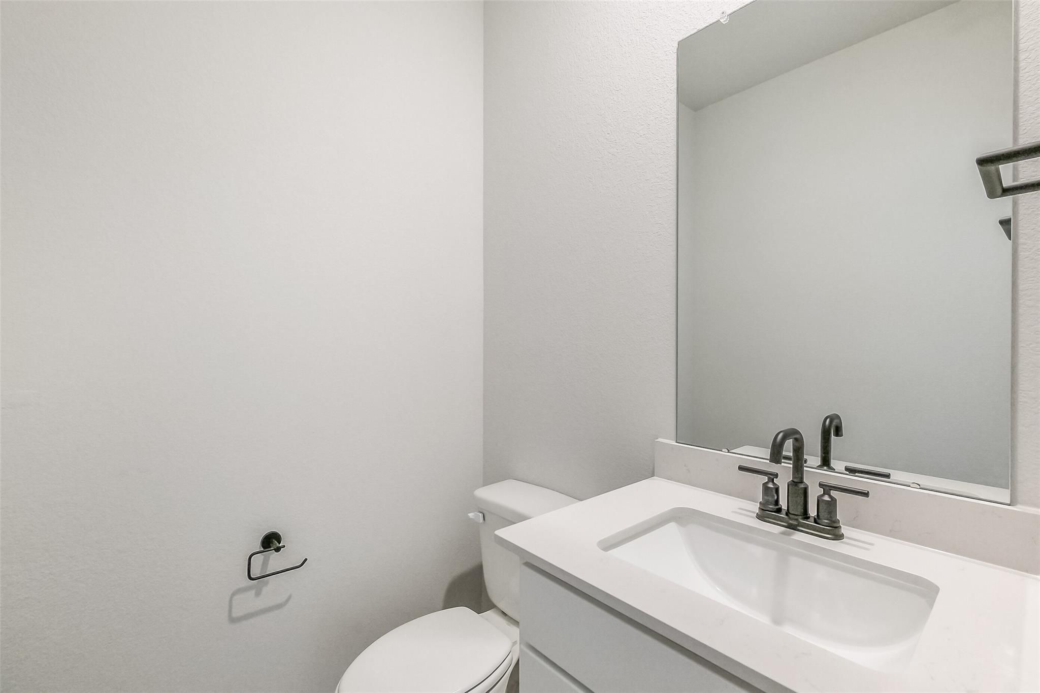 Modern white powder room with sleek vanity sink, chrome faucet, toilet, and large mirror in Davidson Homes Tierra B, Beasley, Texas