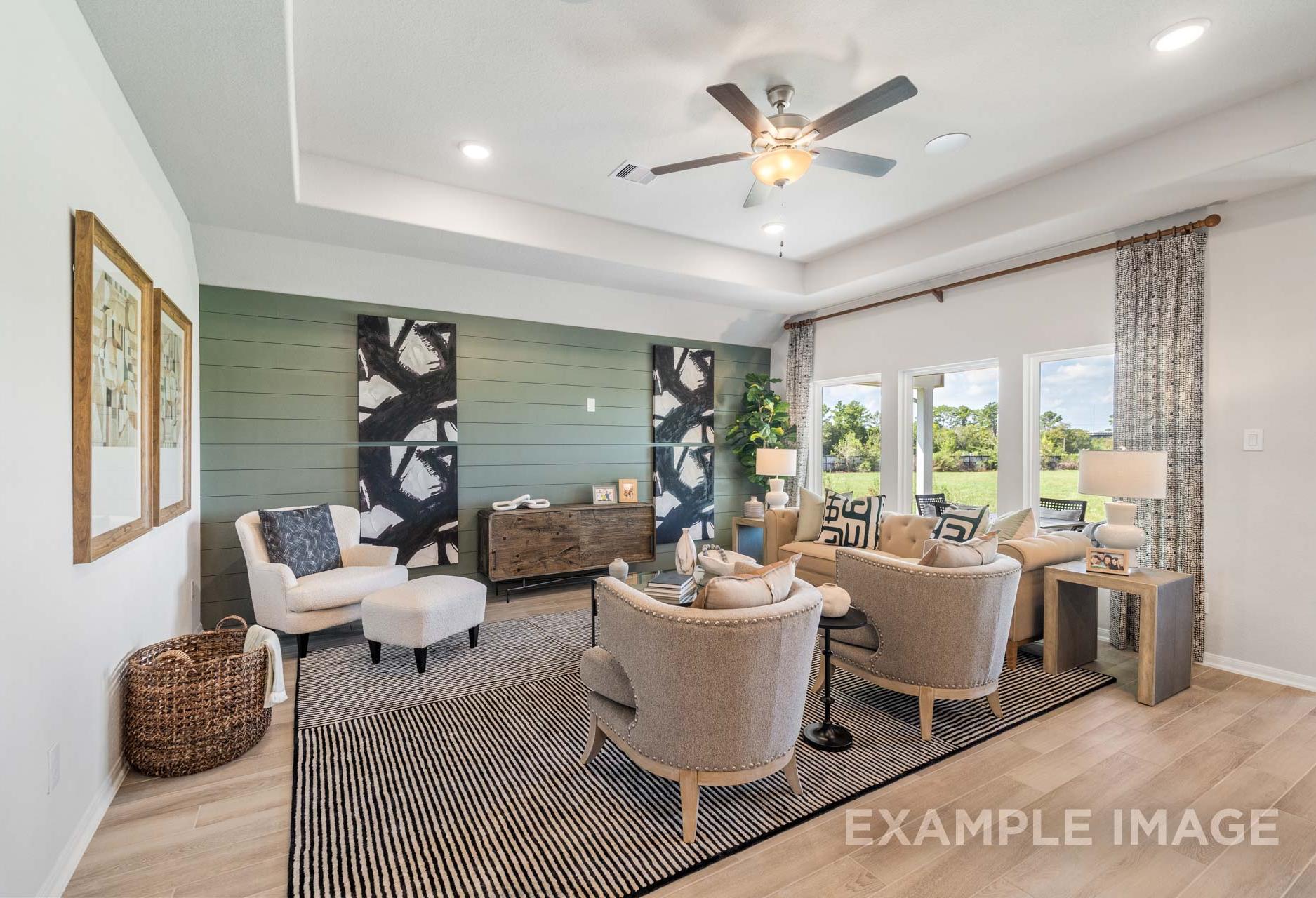 Spacious living room in The Acadia A by Davidson Homes, Rosharon TX: green accent wall, plush armchairs, ceiling fans, large windows to greenery