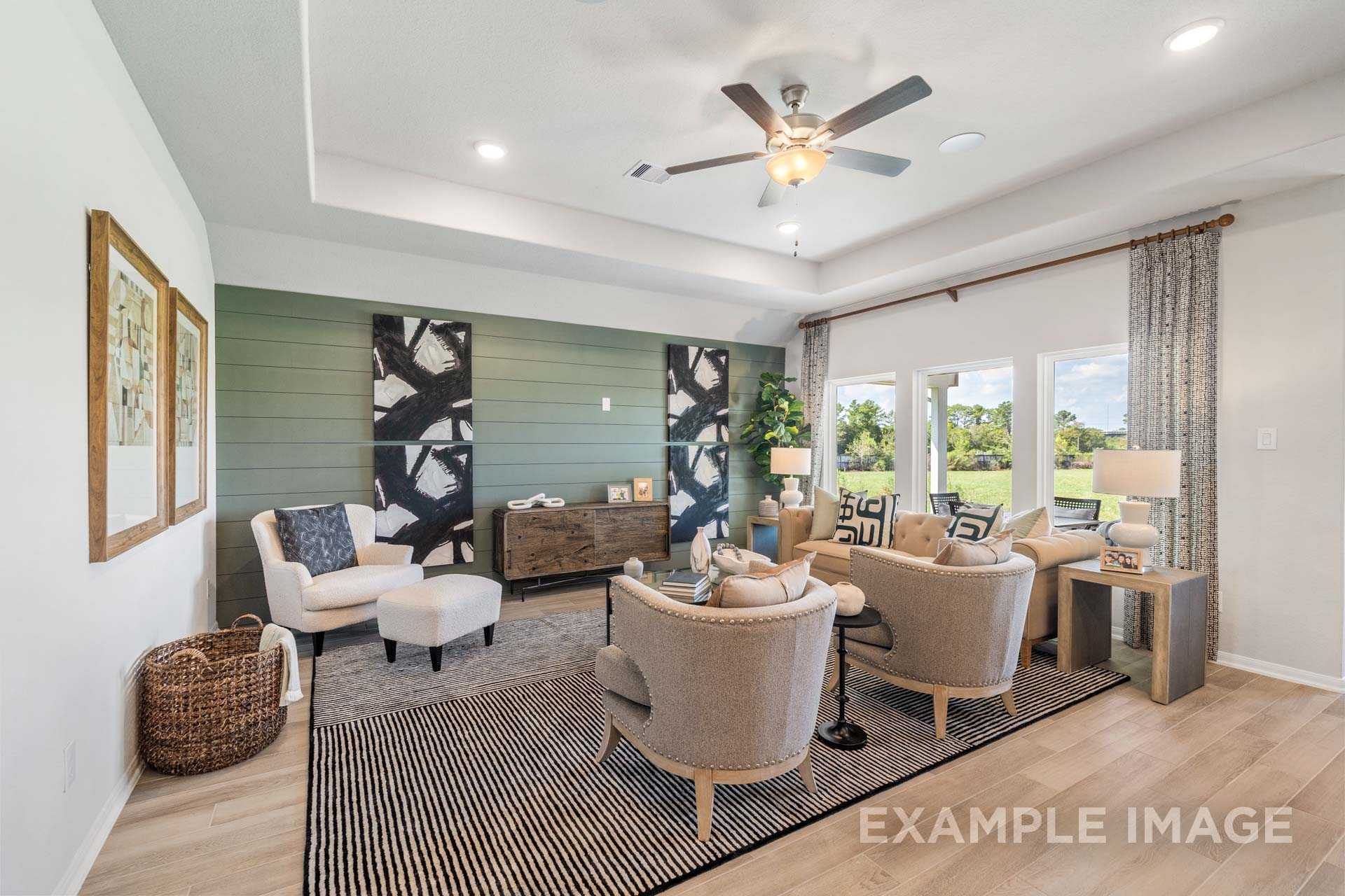 Spacious living room in The Acadia B showcasing modern beige chairs, green accent wall with abstract art, and large windows with greenery views
