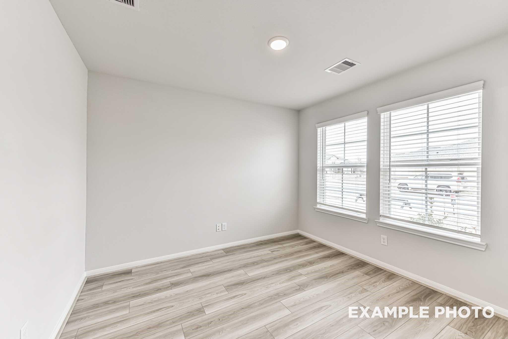 Bright secondary bedroom with light gray walls, double windows with blinds, and luxury vinyl plank flooring in Davidson Homes Riviera A, Rosharon TX