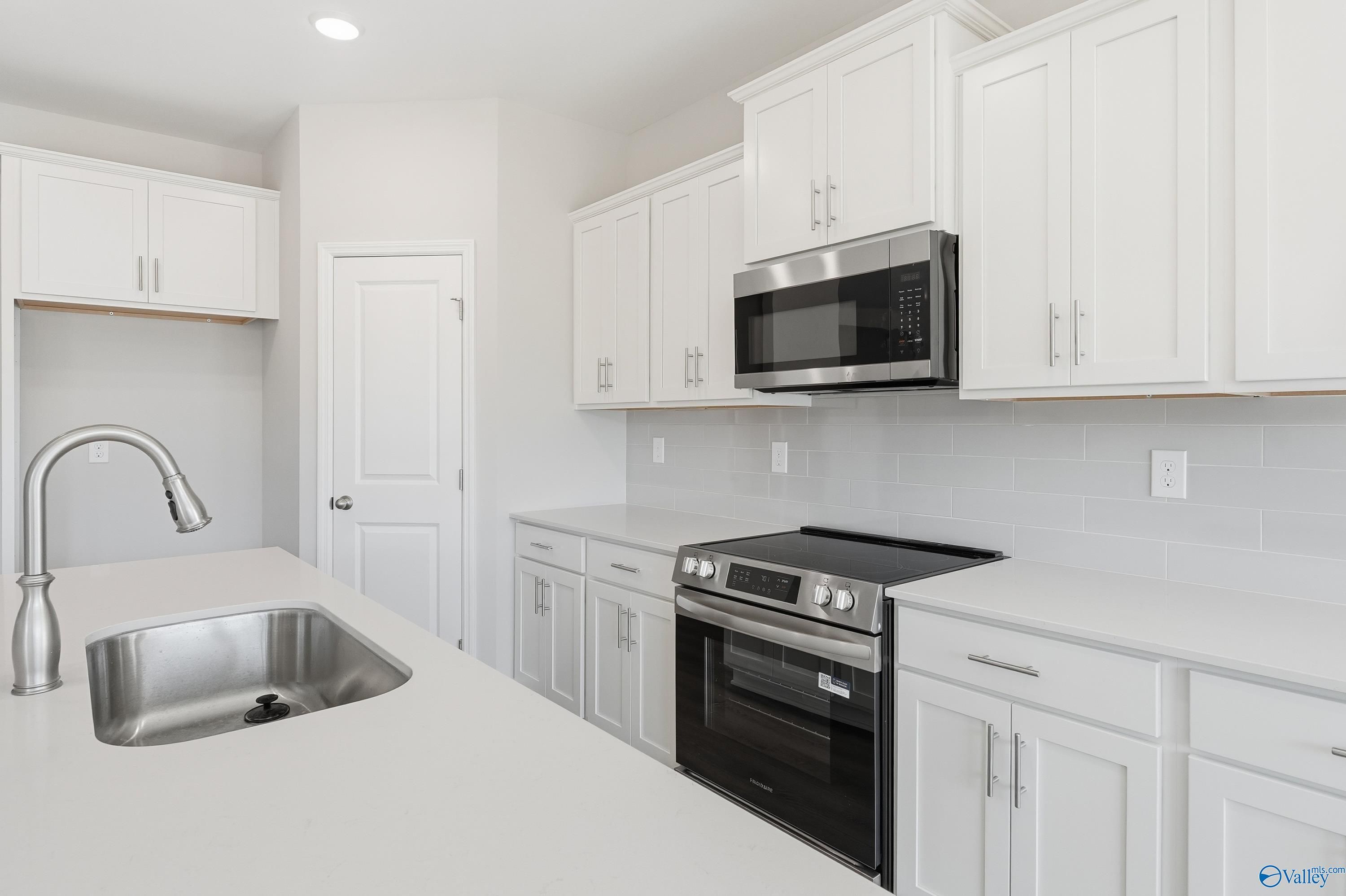 Modern white kitchen featuring stainless steel appliances, quartz counters, and subway tile backsplash in Davidson Homes The Montgomery B, Toney, AL
