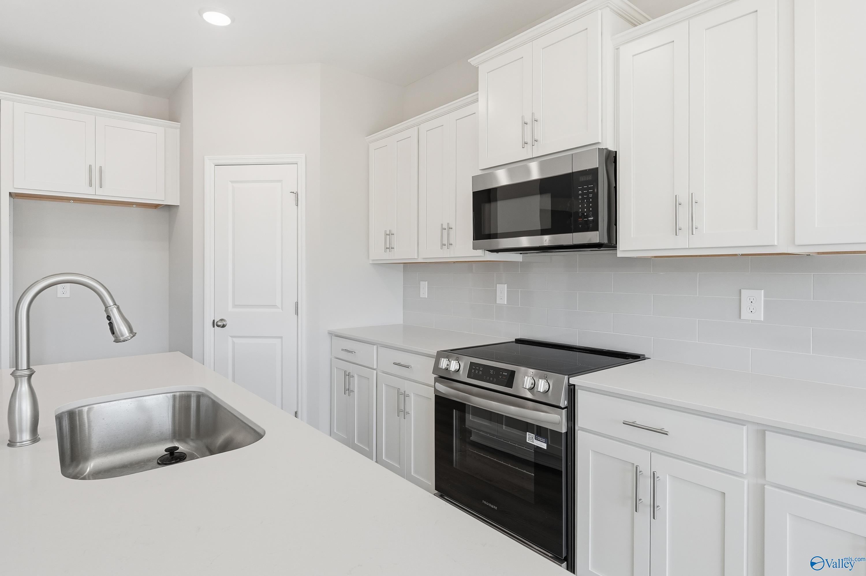 Modern white kitchen with stainless steel appliances, island sink, and subway tile backsplash in Davidson Homes Montgomery B, Toney, AL