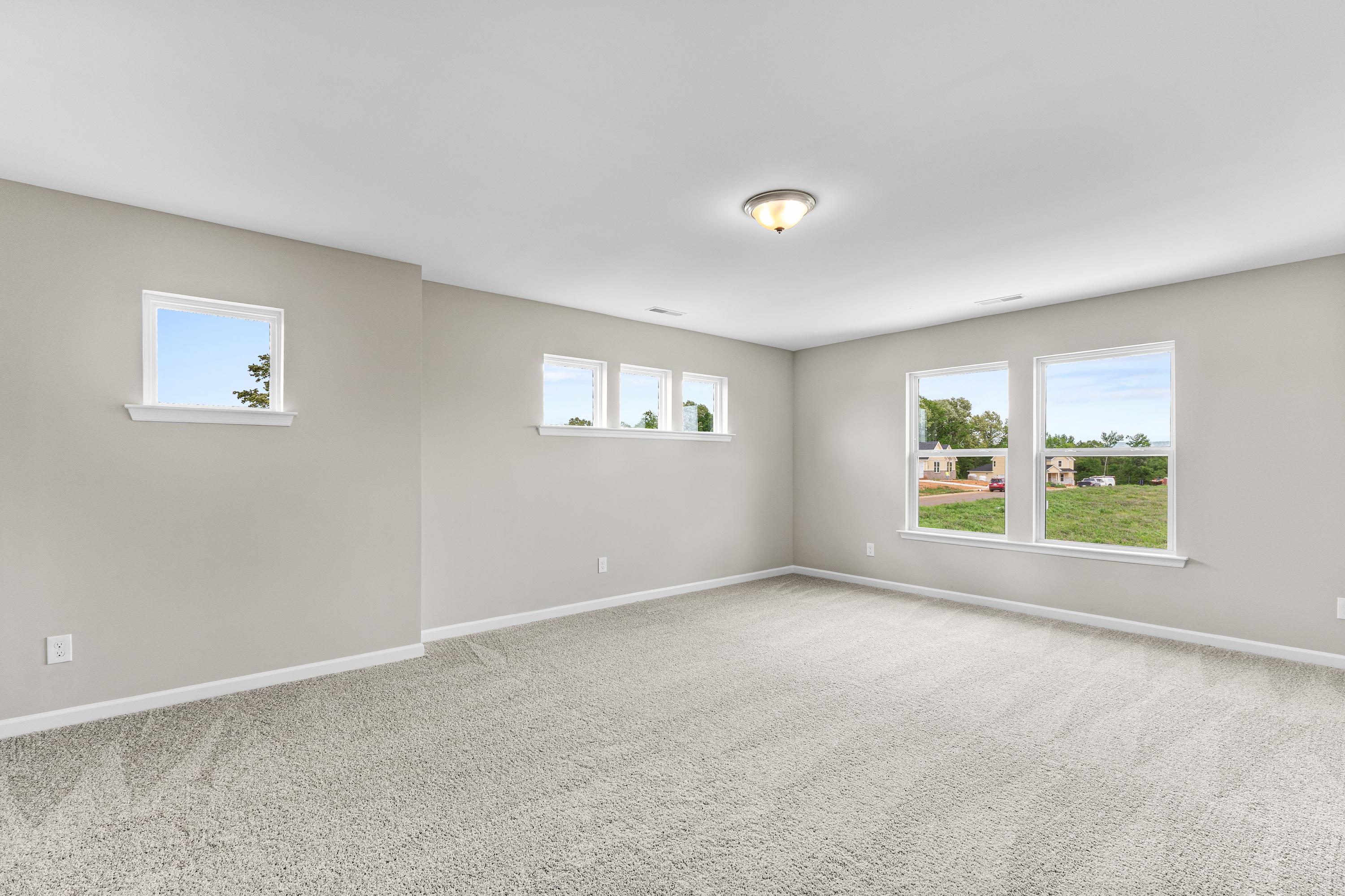 Spacious empty bedroom in The Haven E by Evermore Homes with light gray walls, beige carpet, large windows overlooking green lawn