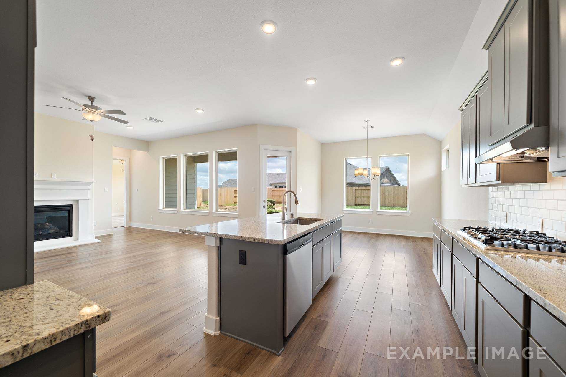 Spacious open-concept kitchen and living area in The Diana C home, featuring dark cabinets, large island, gas fireplace, and hardwood floors