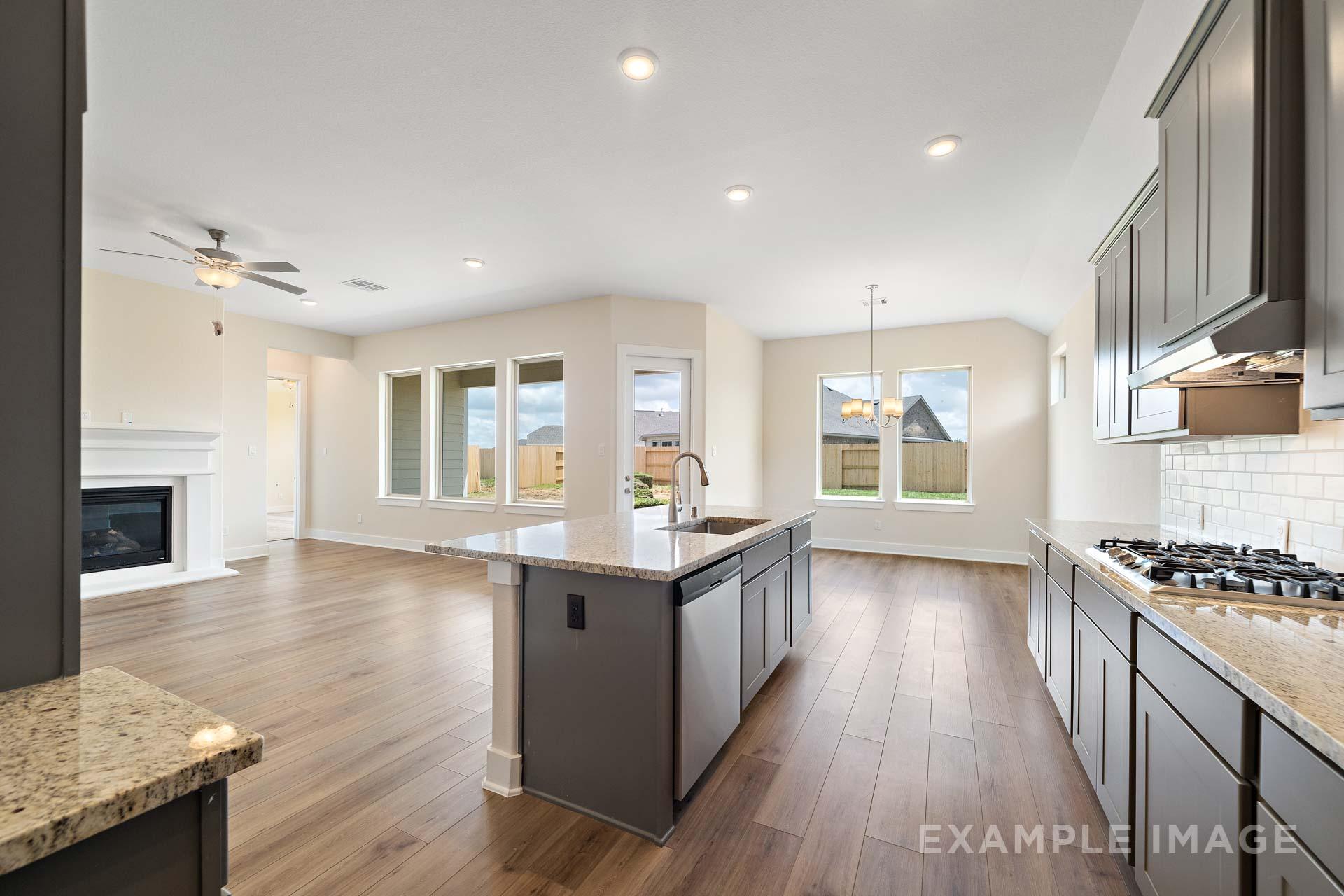 Spacious open-concept kitchen and living area in The Diana C home, featuring dark cabinets, large island, gas fireplace, and hardwood floors