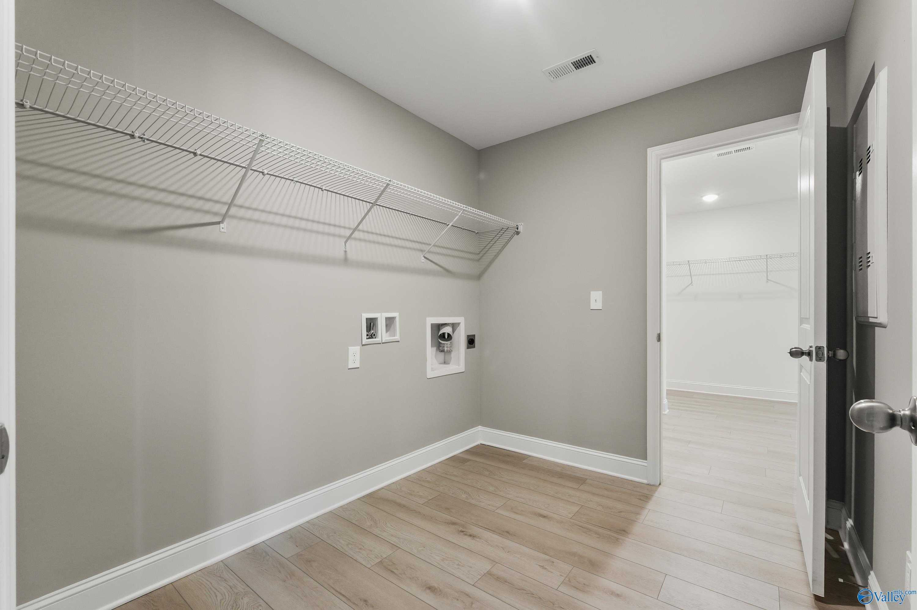Functional laundry room with wire shelving, washer dryer hookups, gray walls, and laminate wood floors in Davidson Homes The Everett B, Athens AL