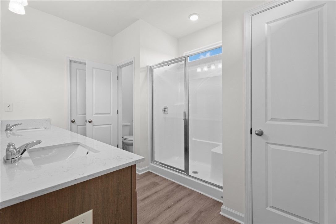 Modern master bathroom with double vanity, walk-in shower, and wood-style flooring in The Stella D at Silver Oak, Cusseta.