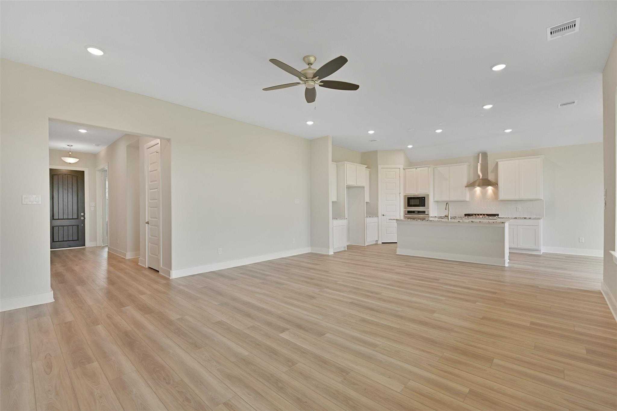 Open-concept living-kitchen with wood floors, white island cabinets, stainless appliances, and ceiling fan in Davidson Homes The Edward A, Lago Mar, Texas City