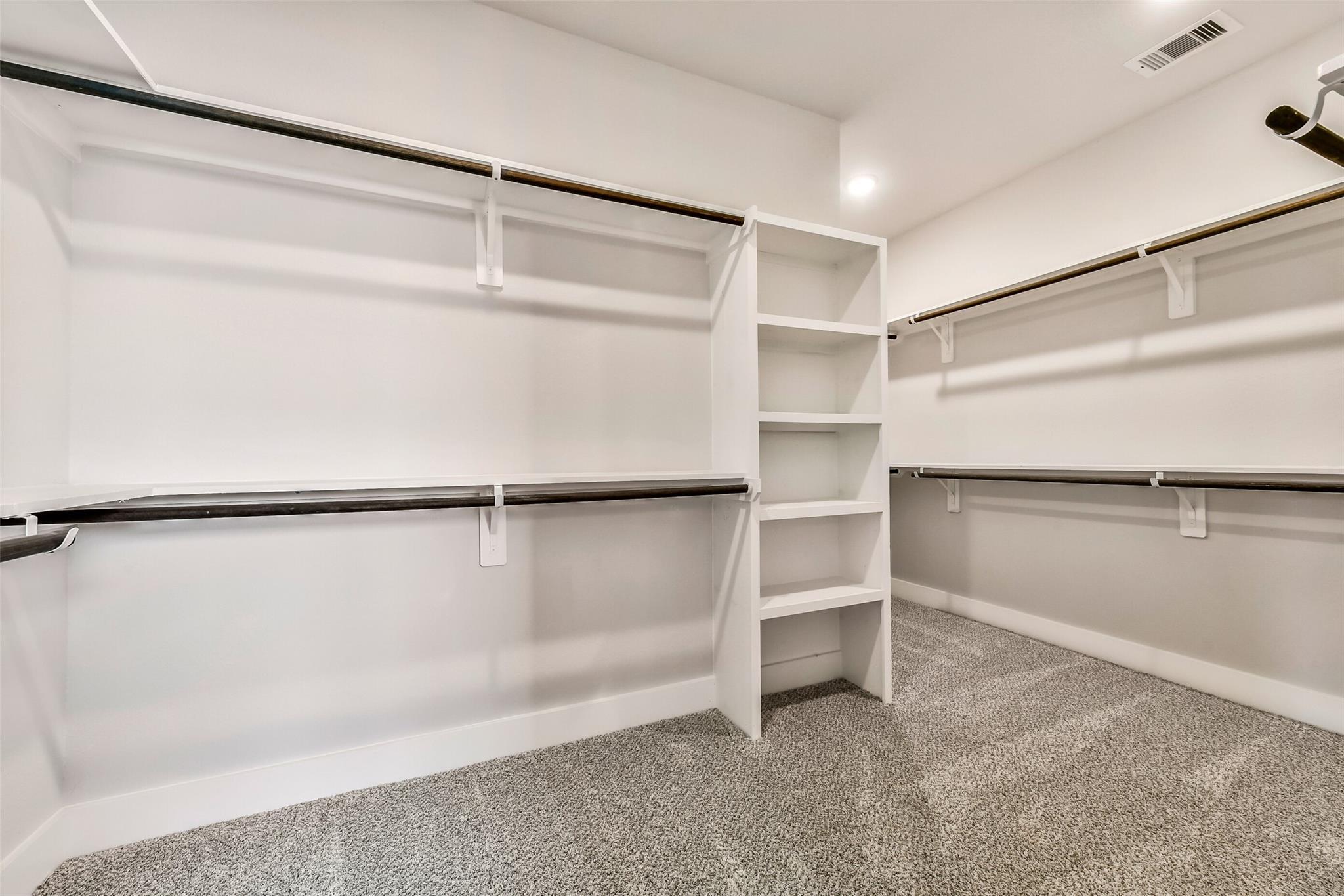 Spacious walk-in closet with white built-in shelves, hanging rods, and gray carpet in Davidson Homes Victoria A, Lago Mar, Texas City