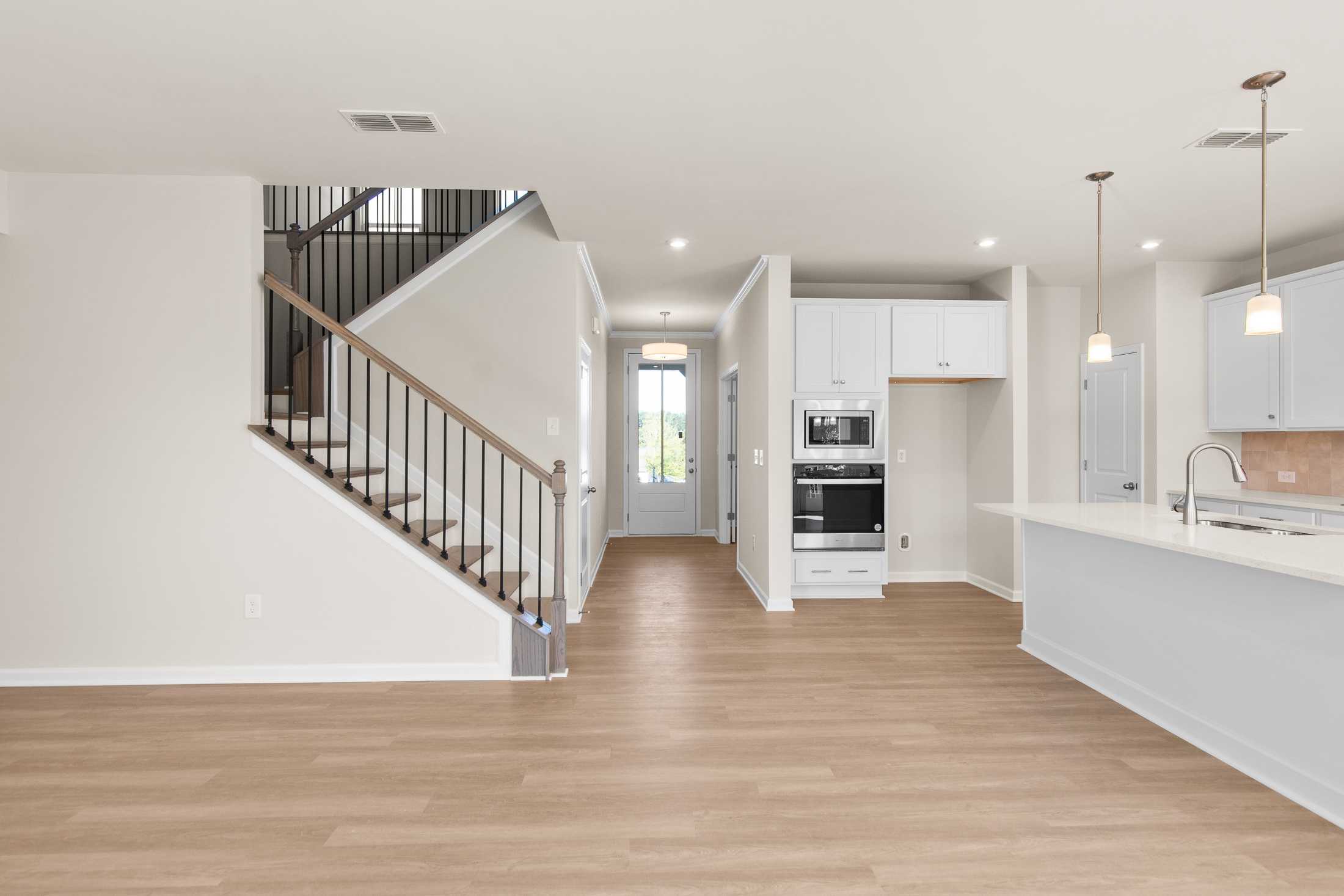 Spacious open-concept interior of The Willow B showcasing wooden staircase, hallway, and white kitchen island in Hoschton Georgia 2-story home