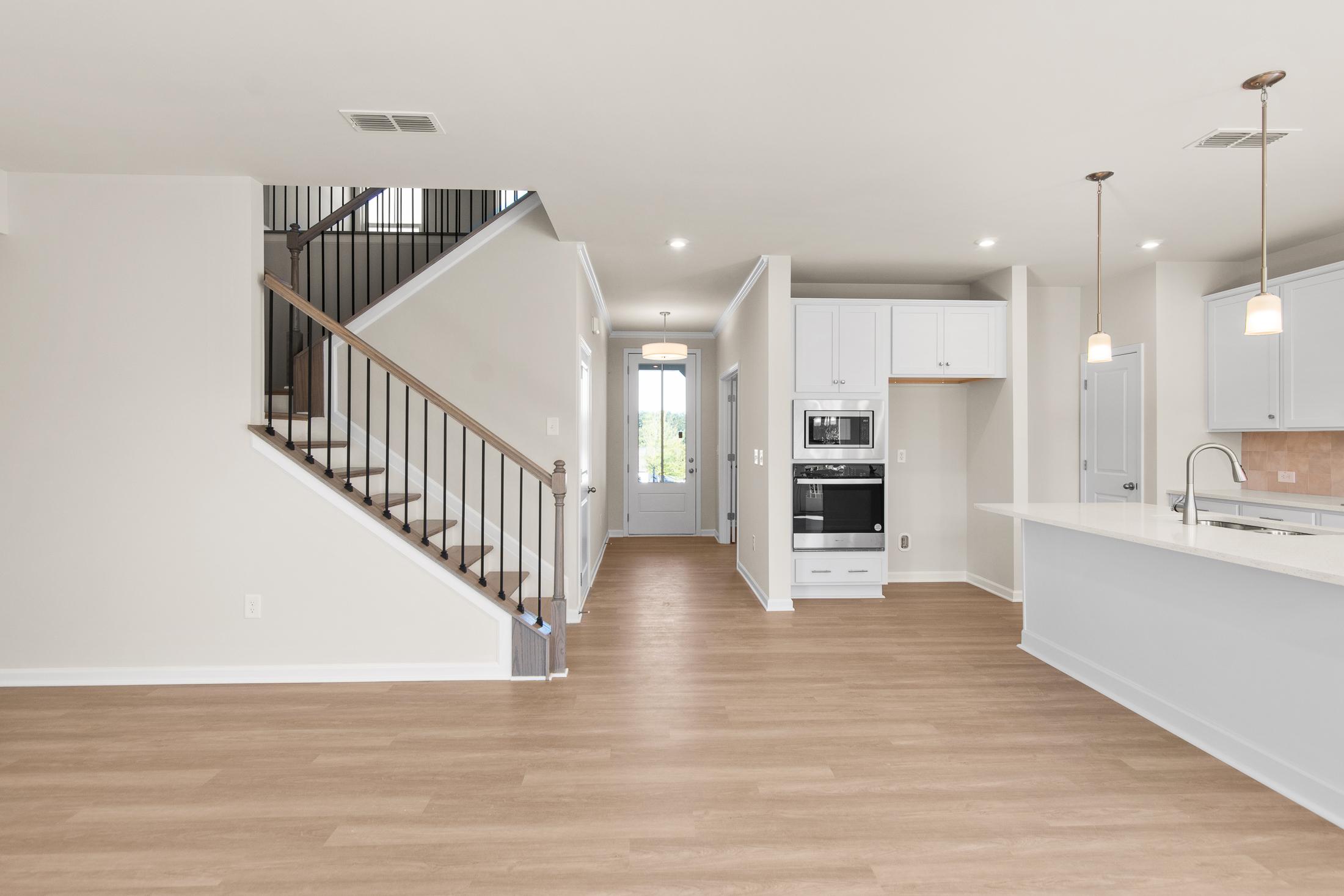 Spacious open-concept interior of The Willow B showcasing wooden staircase, hallway, and white kitchen island in Hoschton Georgia 2-story home