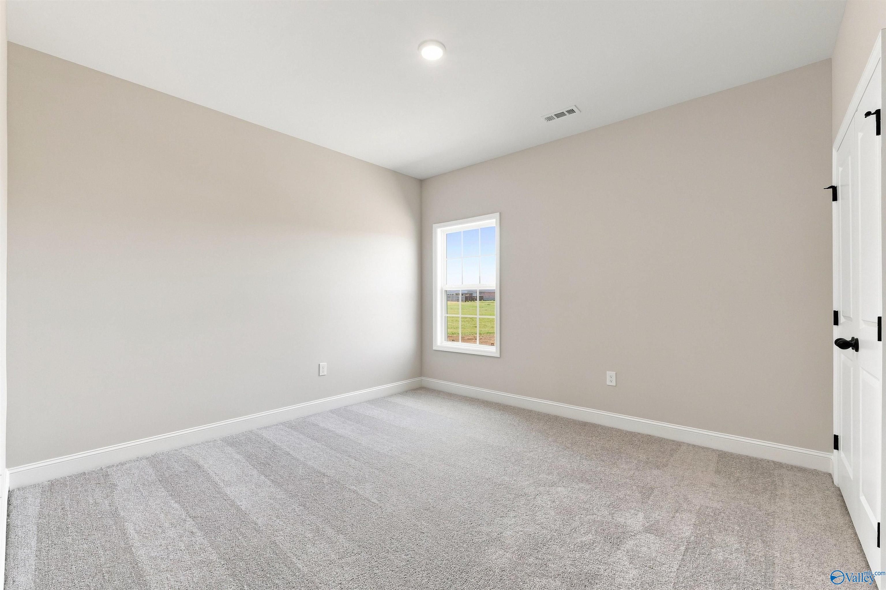 Spacious, neutral-toned bedroom with plush carpeting in The Oxford floor plan home at Kendall Farms in Toney, Alabama.