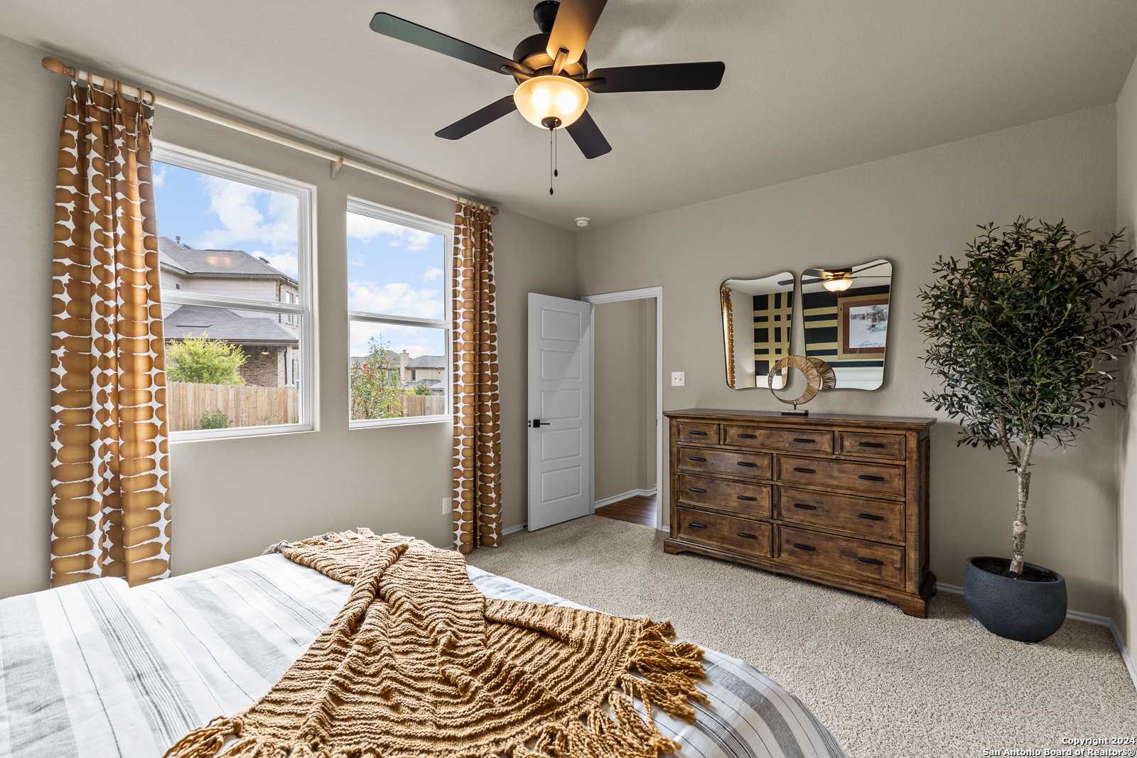 Cozy bedroom with queen bed, knitted throw, wooden dresser, potted plant, ceiling fan in Davidson Homes The Douglas F, San Antonio