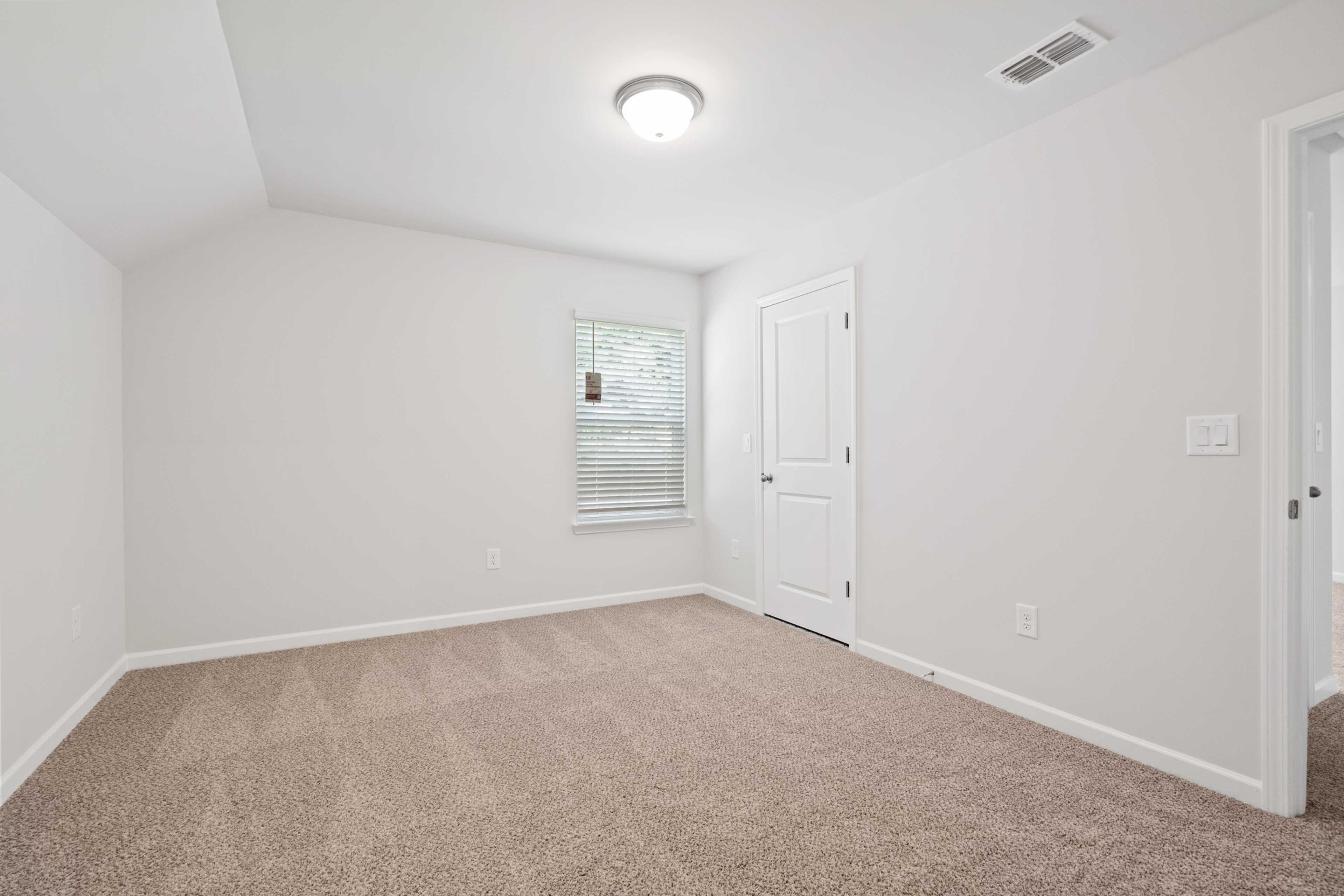 Spacious empty bedroom at Mountainbrook in Cartersville GA with beige carpet, white walls, sloped ceiling and window blinds