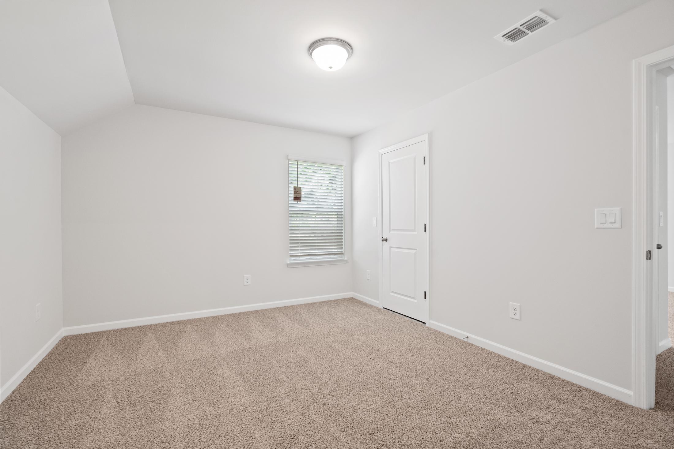 Spacious empty bedroom at Mountainbrook in Cartersville GA with beige carpet, white walls, sloped ceiling and window blinds