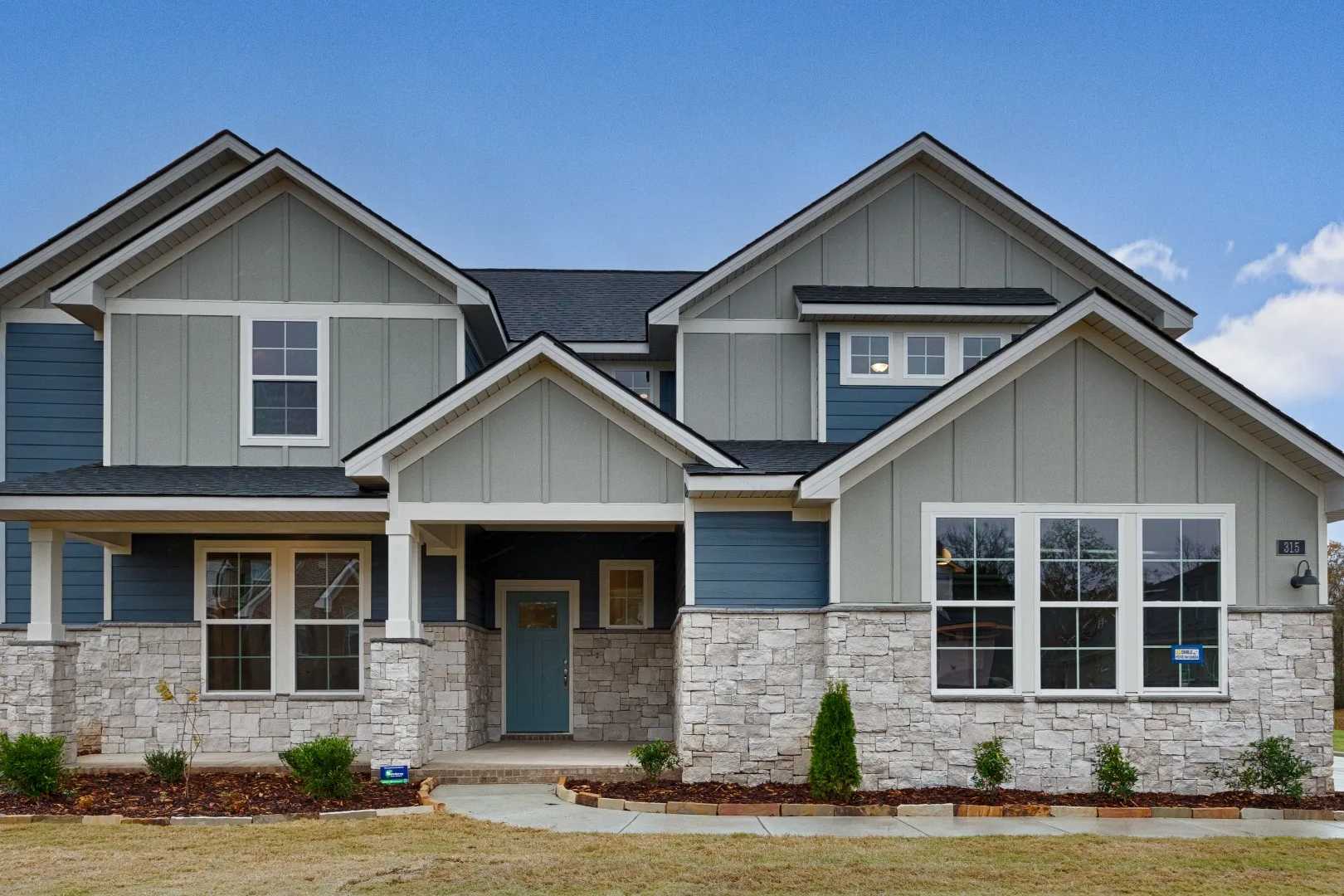 Contemporary blue-sided two-story home exterior at The Meadows at Hampton Cove, Owens Cross Roads AL with covered porch and stone base