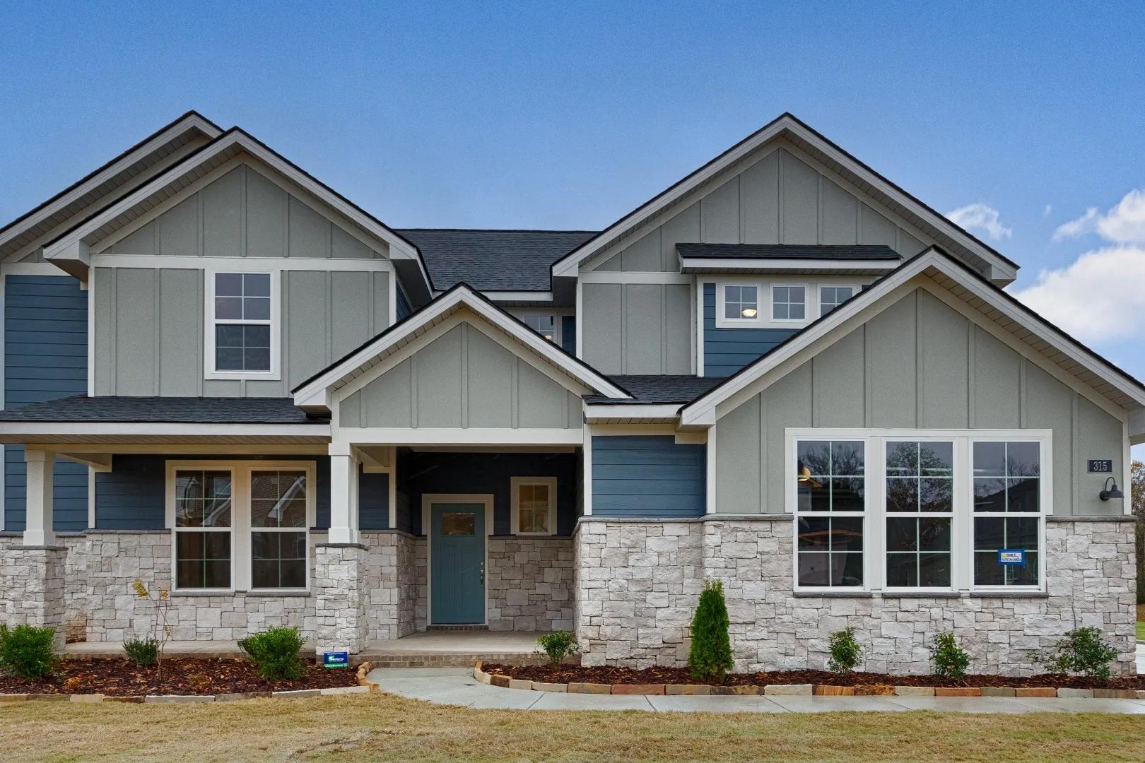 Contemporary blue-sided two-story home exterior at The Meadows at Hampton Cove, Owens Cross Roads AL with covered porch and stone base