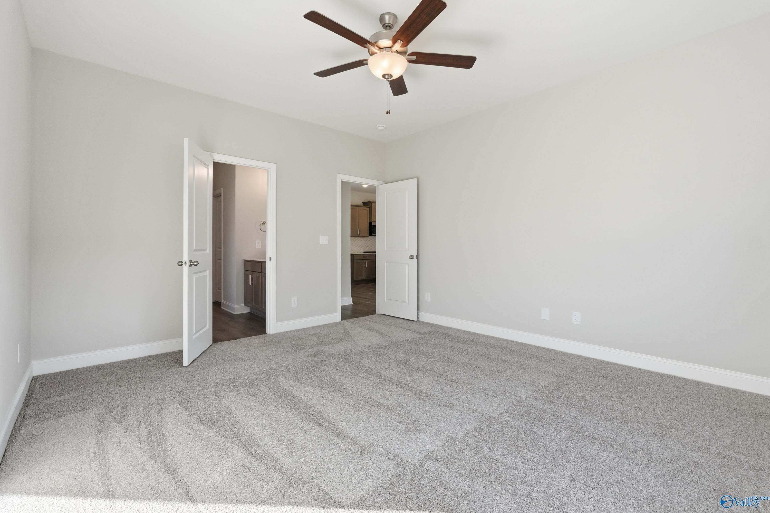 Spacious master bedroom with ceiling fan, open en-suite bath doors, and kitchen view in Davidson Homes The Daphne C, Arab, Alabama