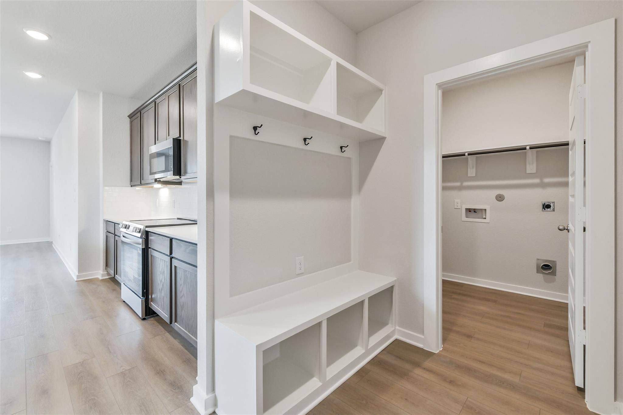 Functional mudroom with white cabinets, coat hooks, bench, and laundry area adjacent to modern kitchen in Davidson Homes Brazos E, Cleveland TX