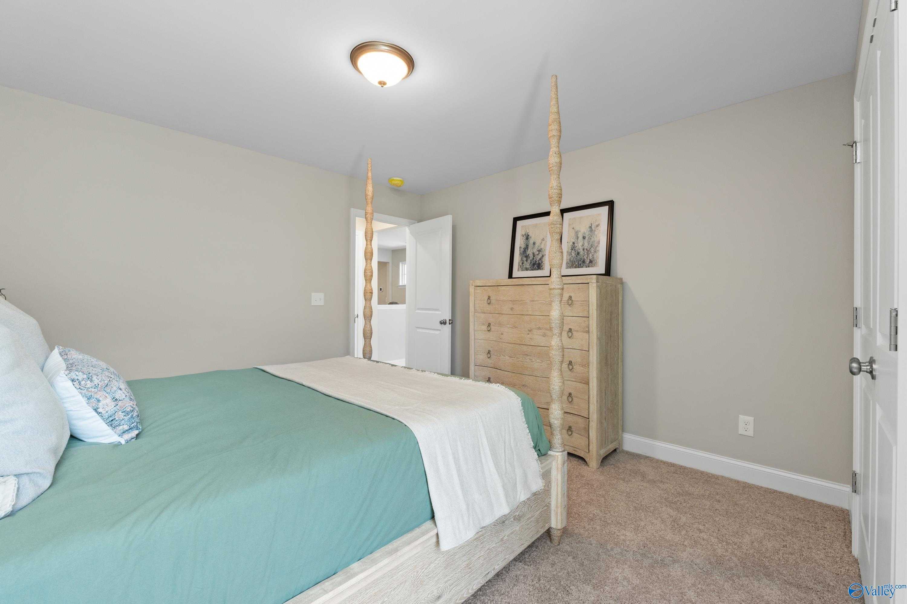 Cozy bedroom with teal four-poster bed, white bedding, wooden dresser in Evermore Homes The Haven, Owens Cross Roads, AL