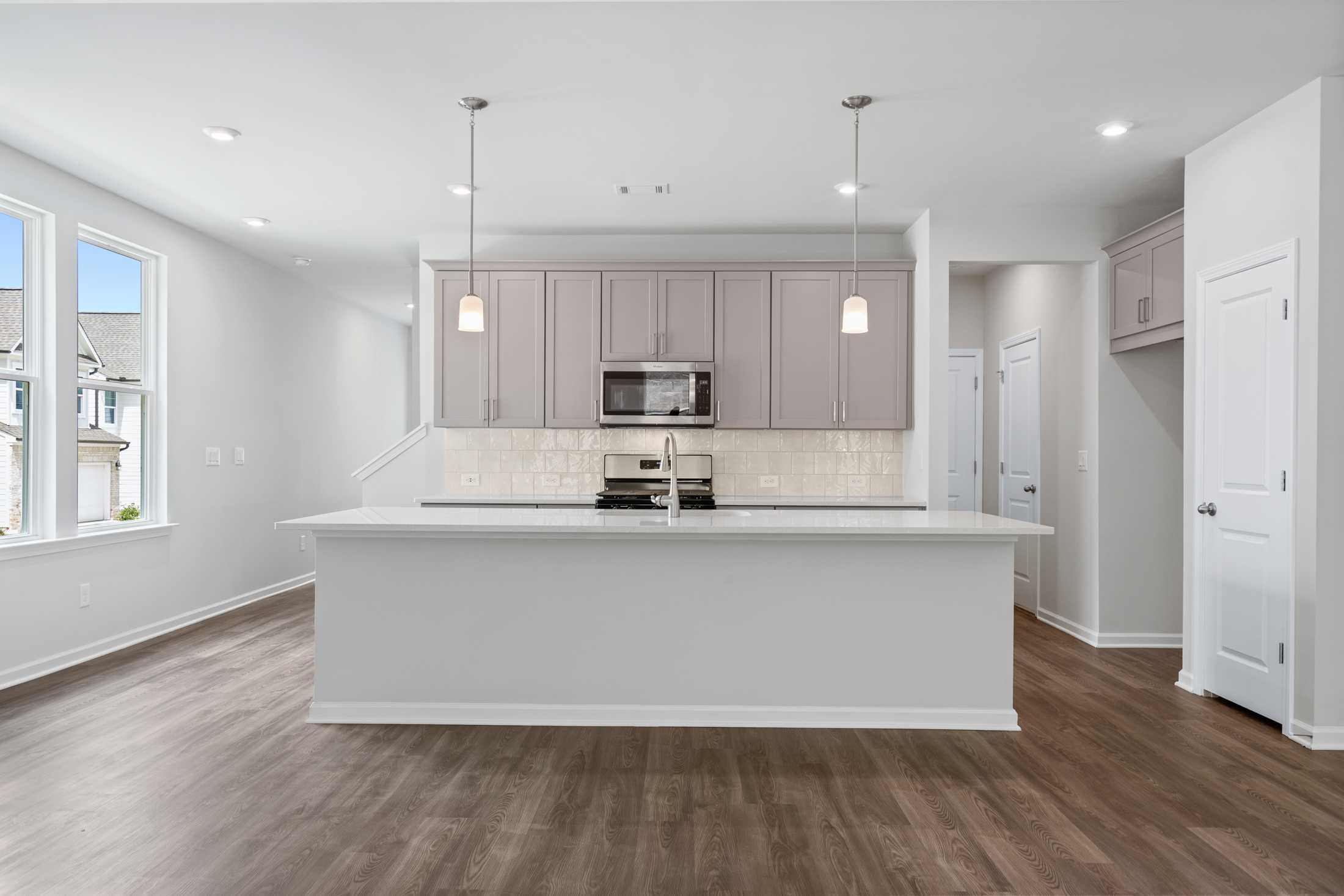 Spacious modern kitchen in The Cary A with white island, shaker cabinets, stainless appliances, and hardwood floors
