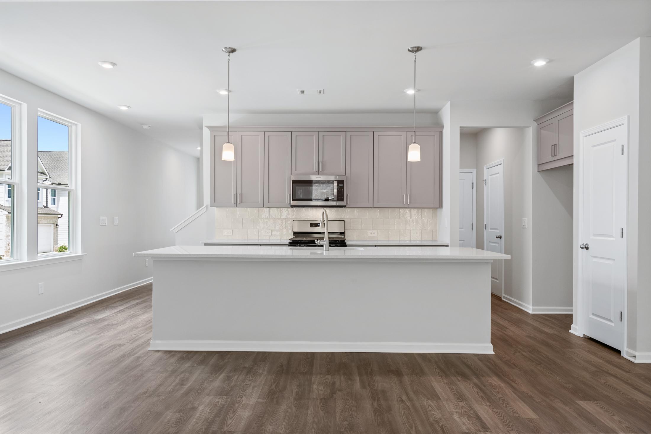 Spacious modern kitchen in The Cary A with white island, shaker cabinets, stainless appliances, and hardwood floors
