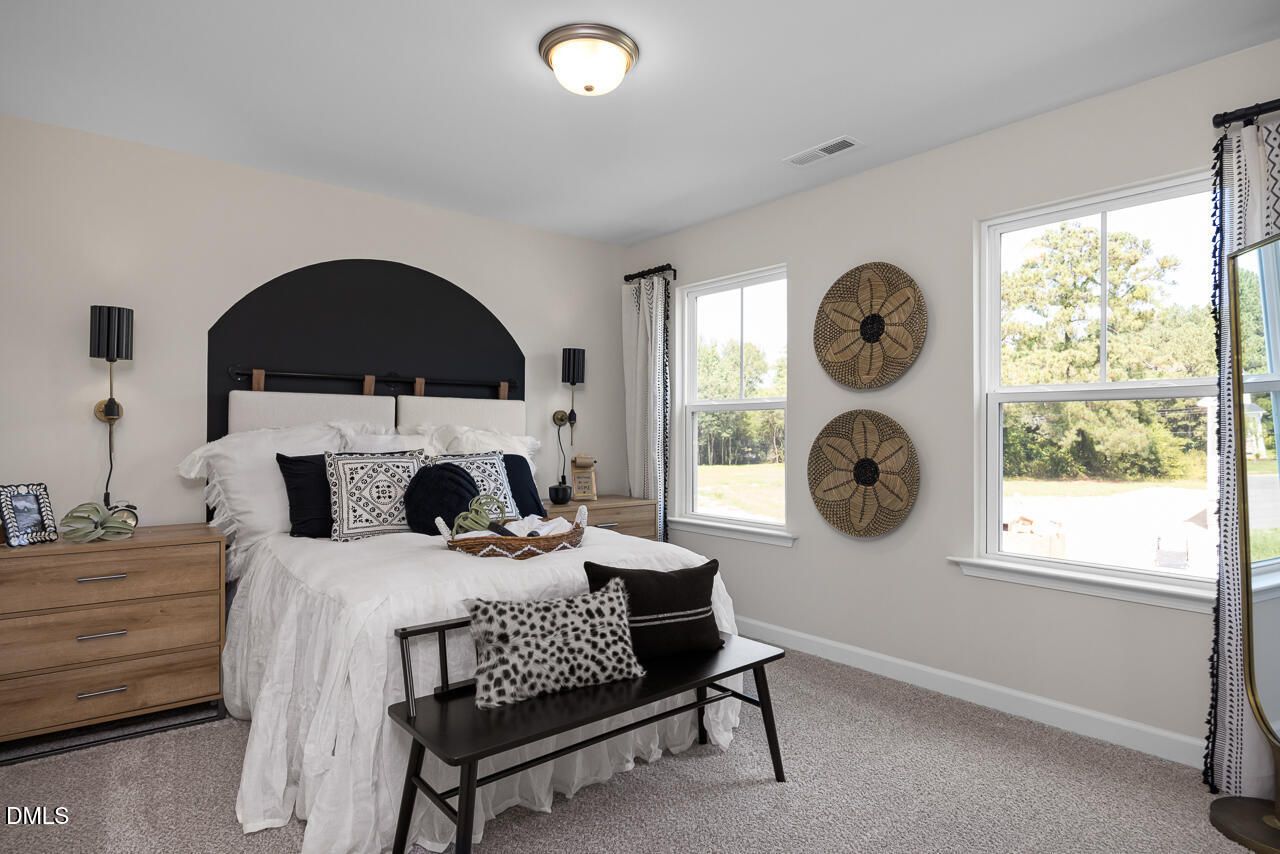 Cozy secondary bedroom with black upholstered headboard, white bedding, woven wall art, and large windows in Davidson Homes The Hickory II C, Zebulon, NC